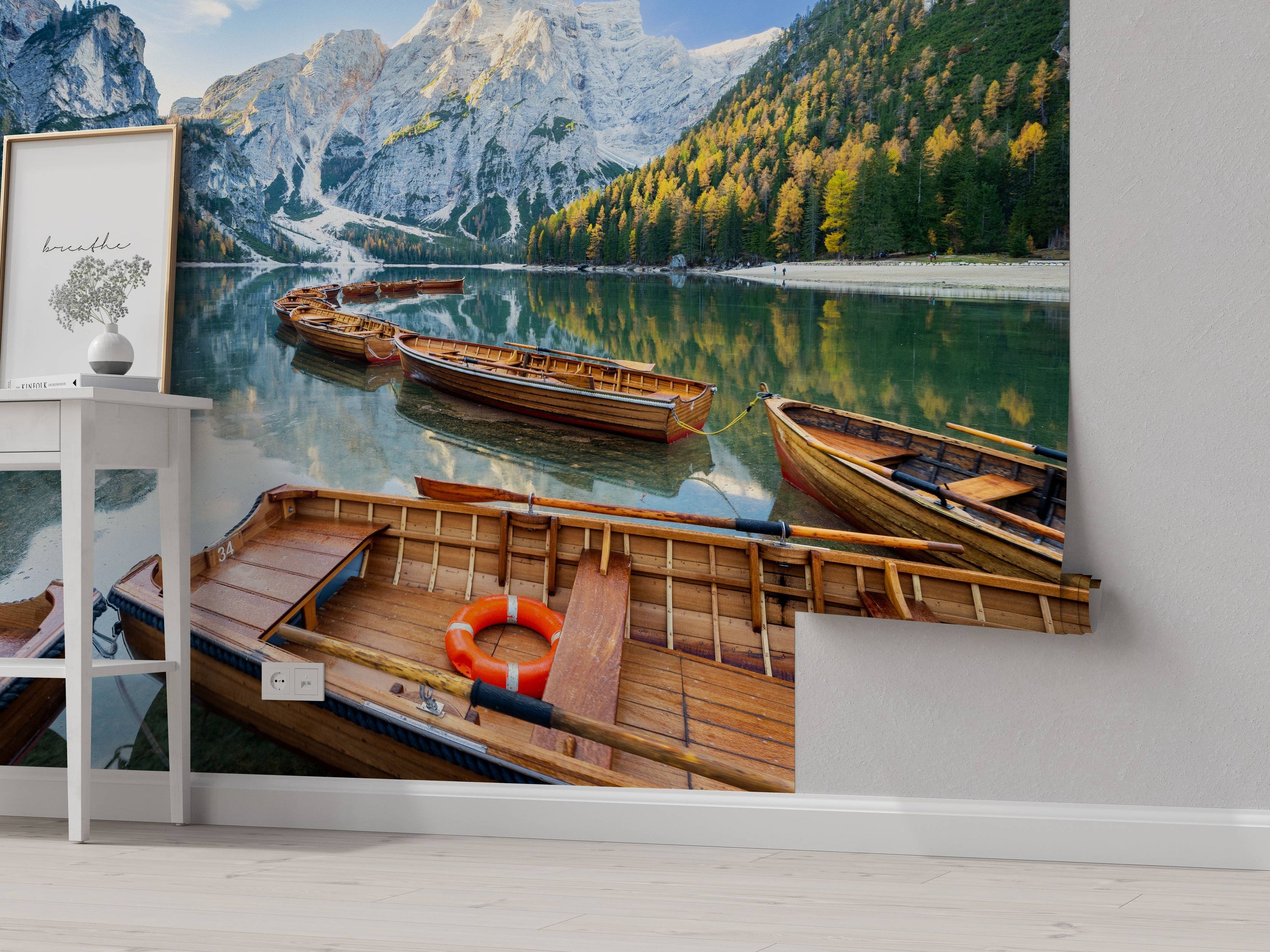 A scenic mural of wooden boats on a calm lake, with snow-capped mountains and a forest with yellow and green trees.