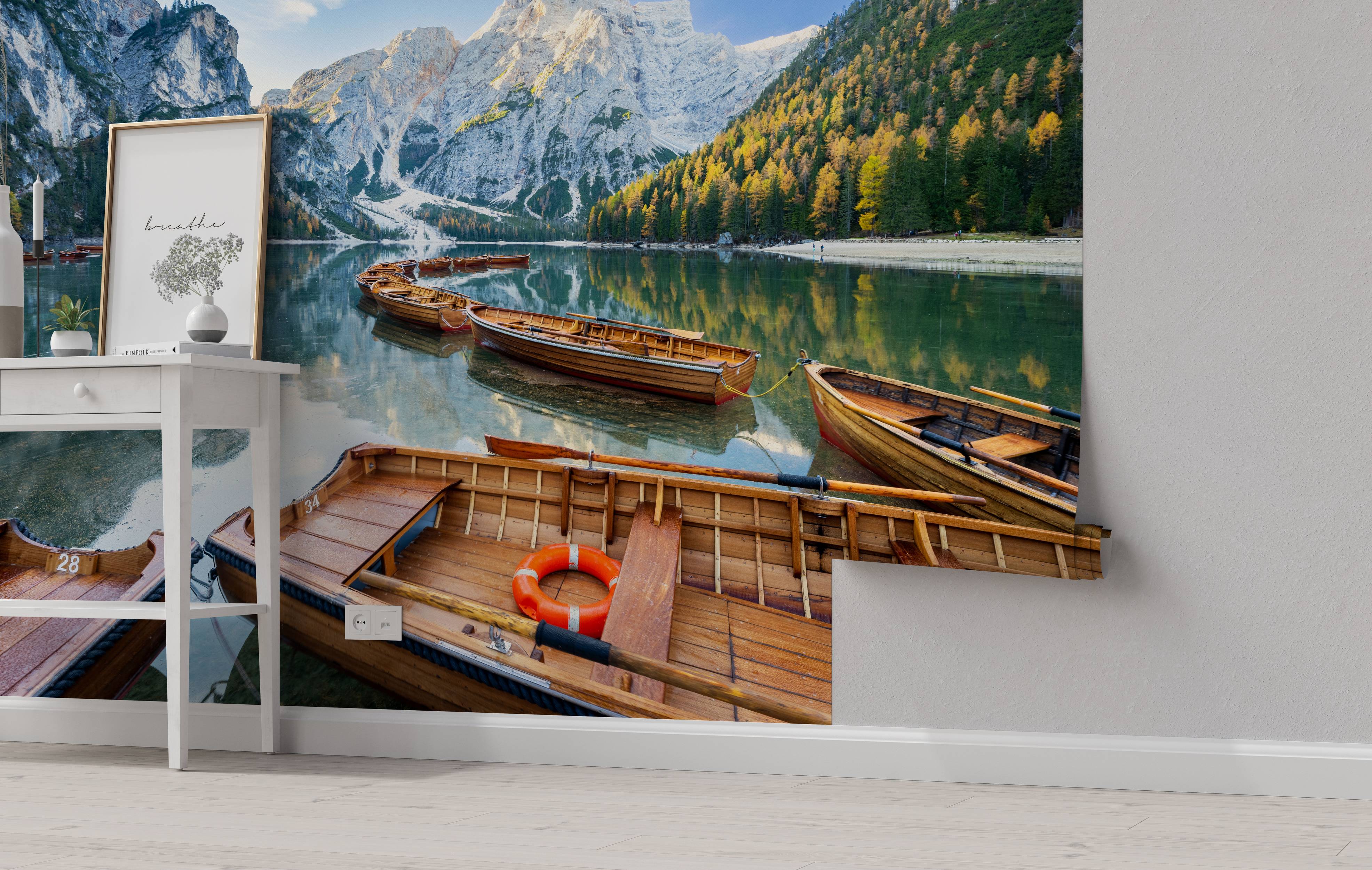 A scenic mural of wooden boats on a calm lake, with snow-capped mountains and a forest with yellow and green trees.