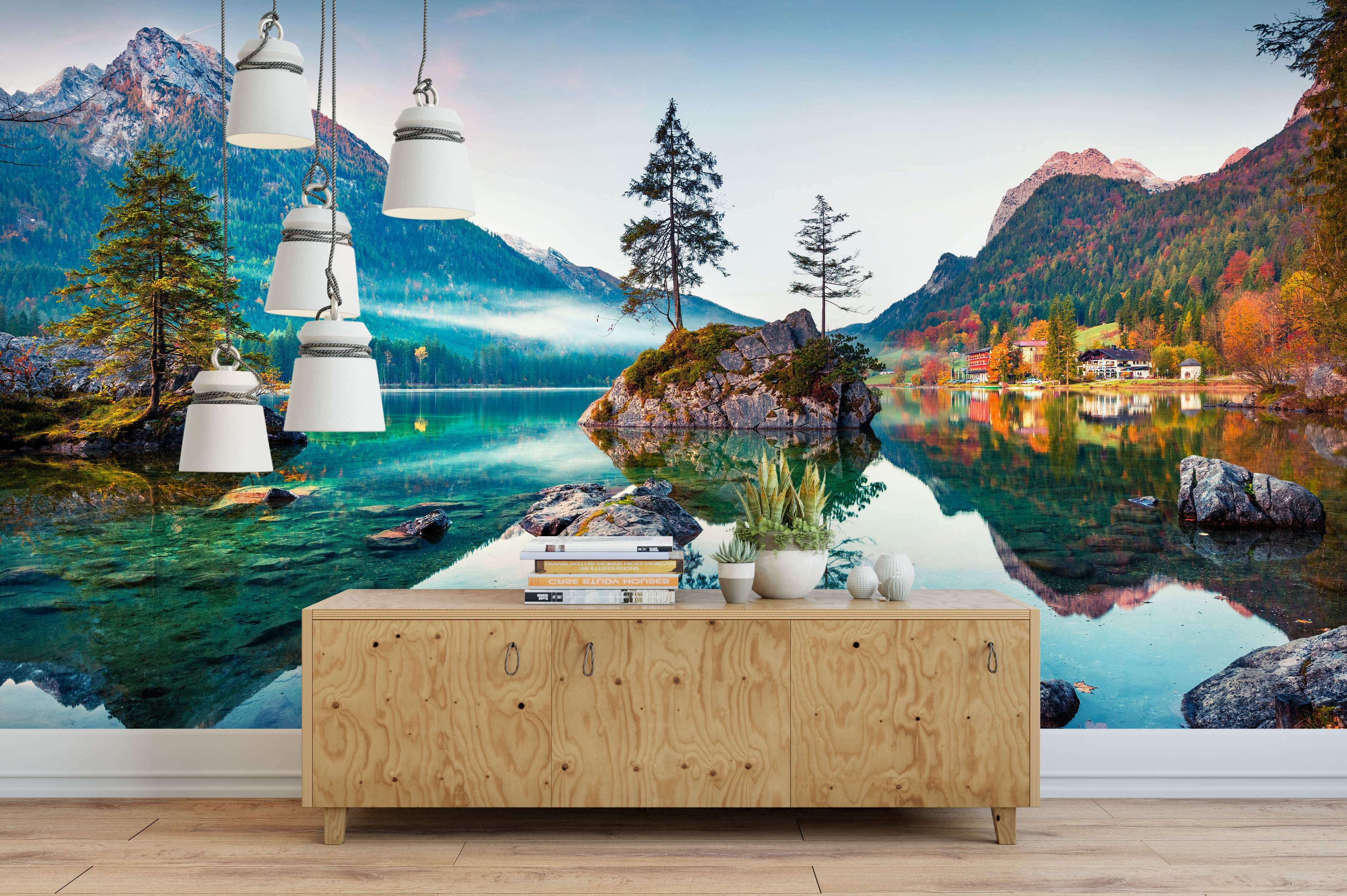 Mountain lake landscape mural with clear turquoise water reflecting autumn mountains and a tree-covered island under a hazy sky.