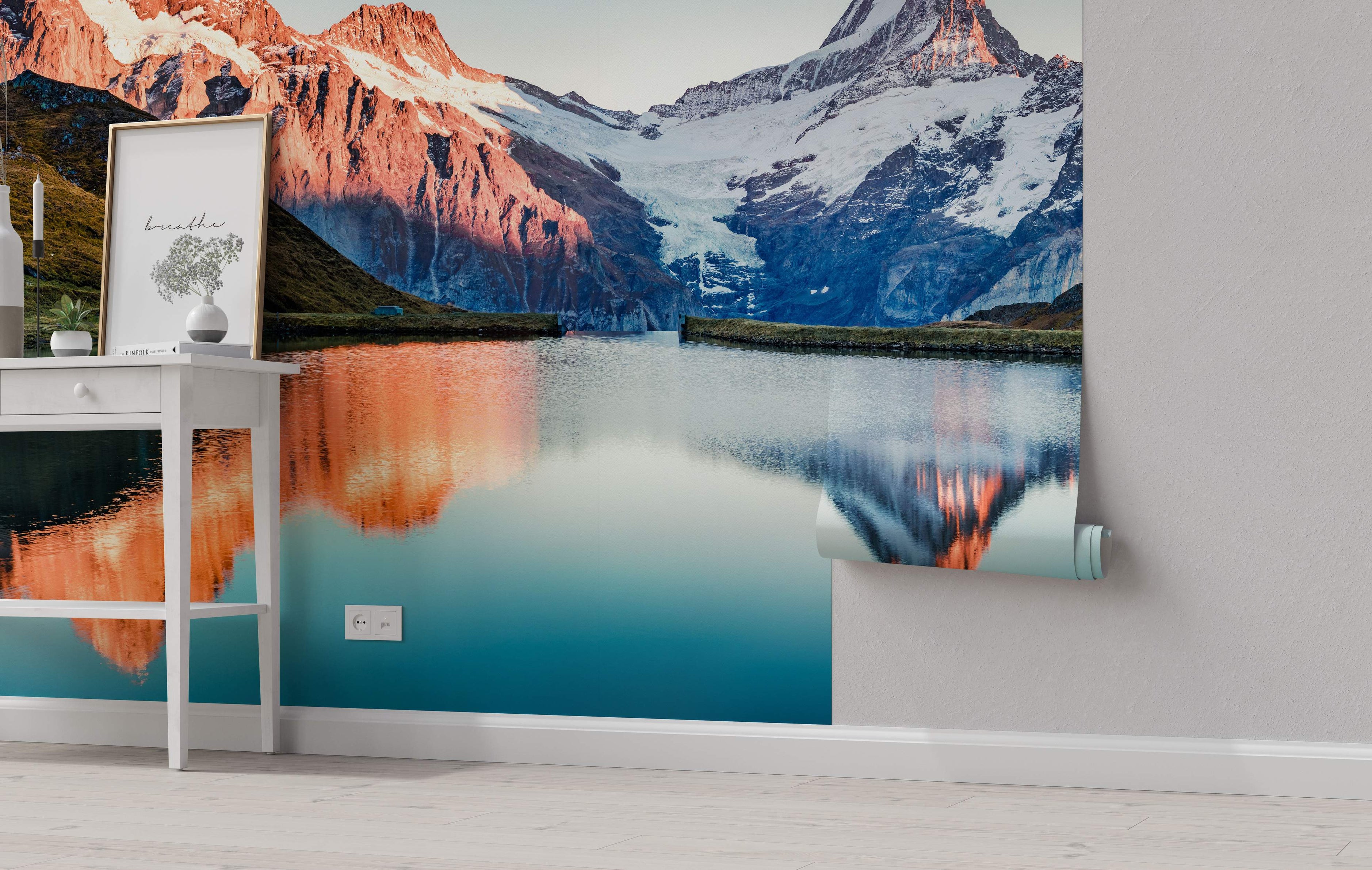 Scenic mural depicting sunlit red mountains and shadowed blue peaks reflected in a tranquil lake with snowy tops.