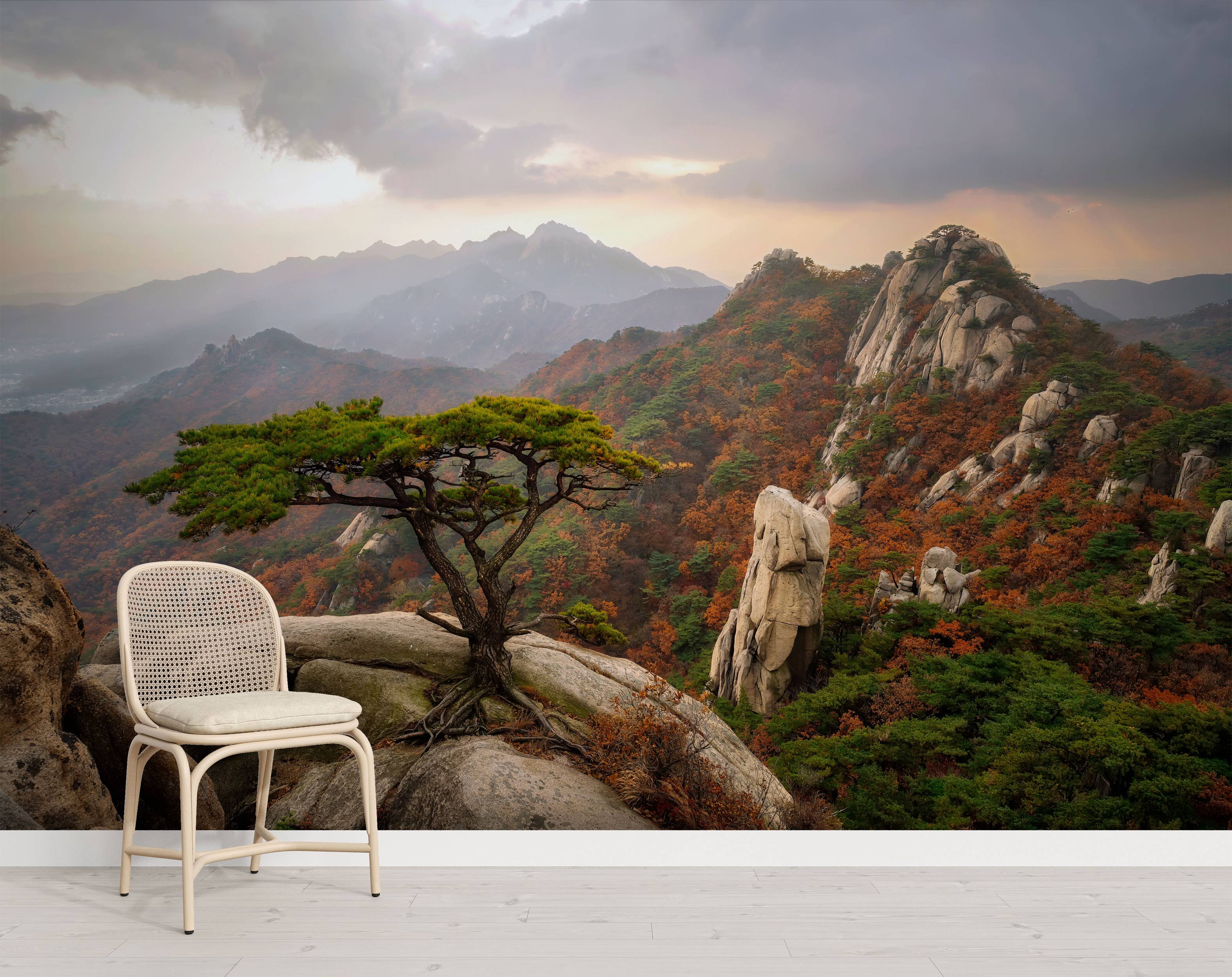 Mural of a rugged mountain landscape in autumn, featuring a lone pine tree on a rocky peak under a dramatic, cloudy sky.