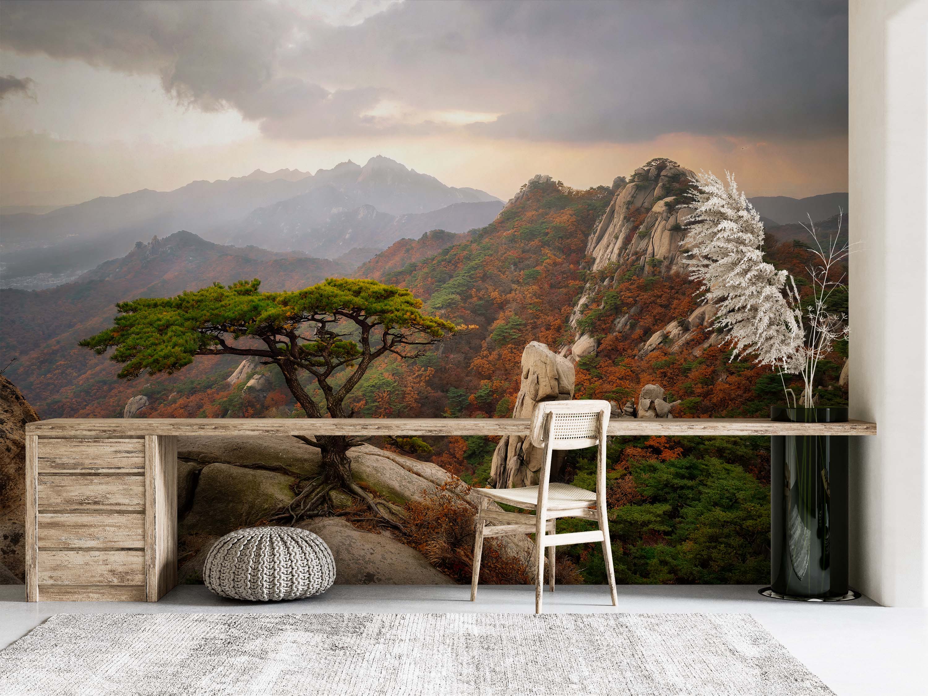 A scenic mountain mural with a pine tree on a rocky cliff. The hills are covered in orange and green autumn trees under a cloudy sky.