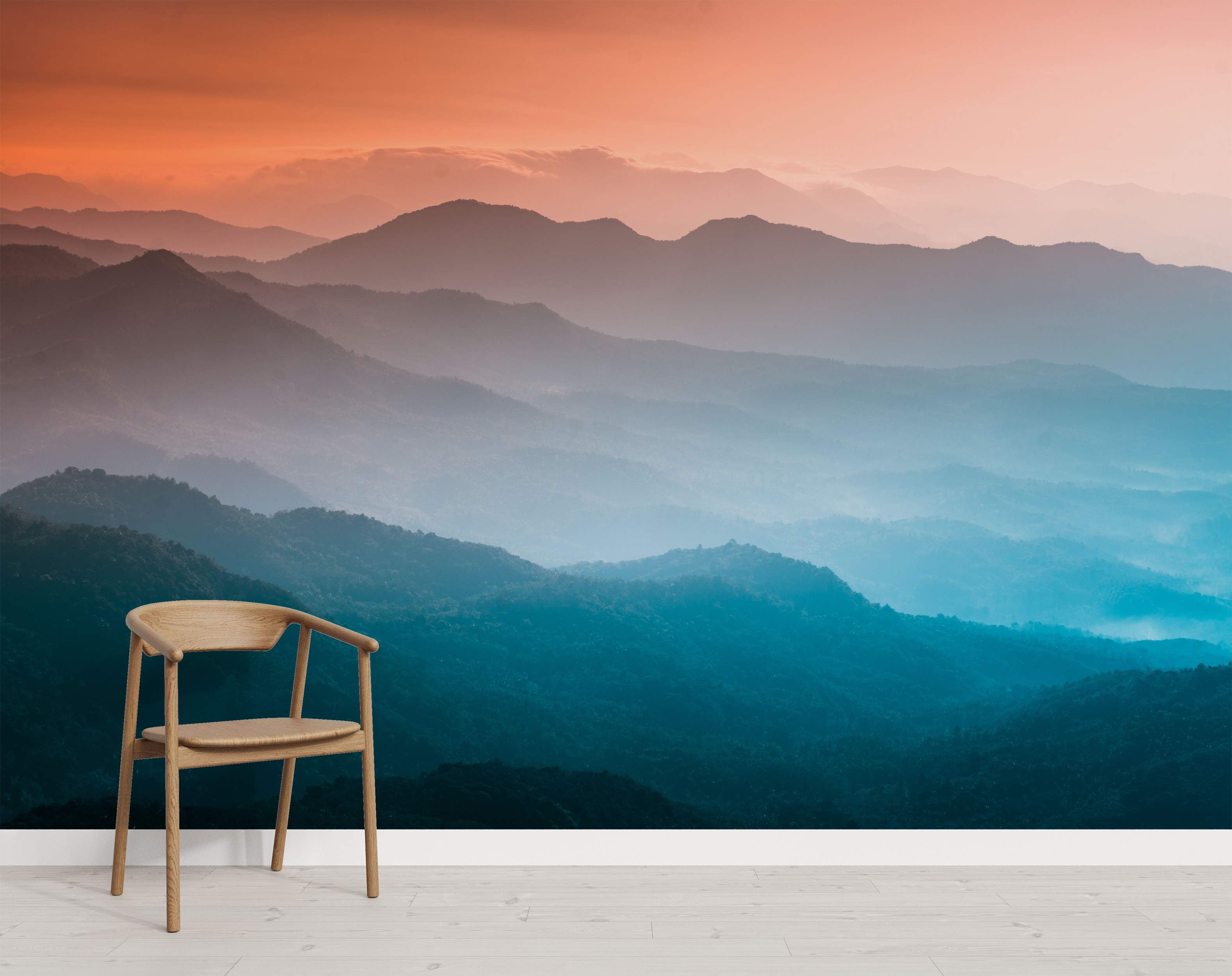 Misty mountain range mural with layered peaks. An orange sunset sky transitions to hazy blue and teal valleys below.