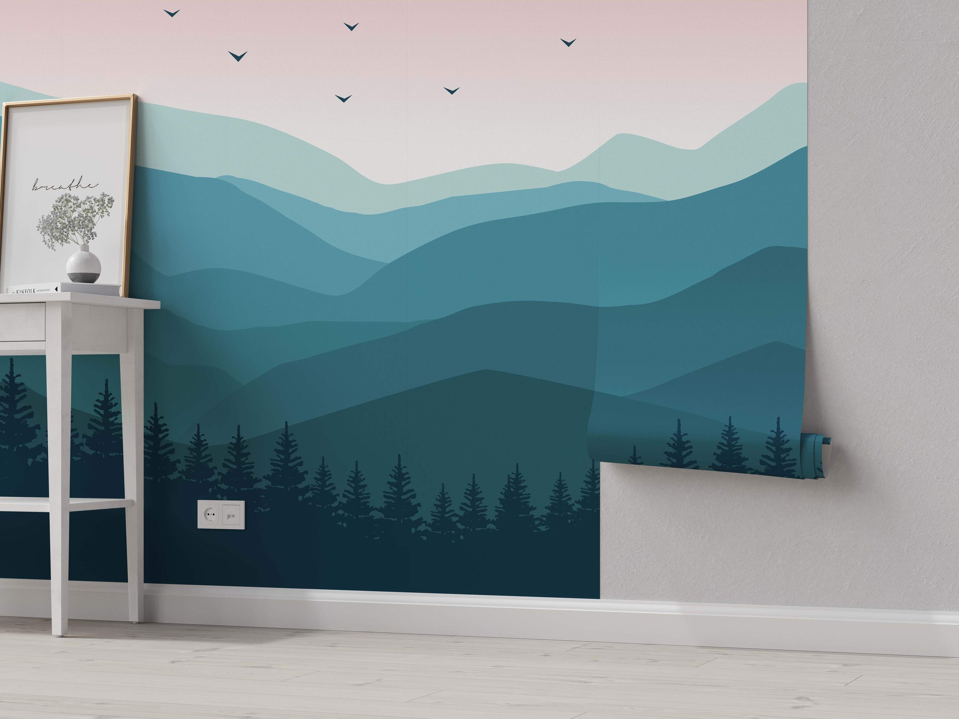 Minimalist landscape mural featuring layered teal and blue mountains, a dark forest silhouette, and a pale pink sky with bird silhouettes.