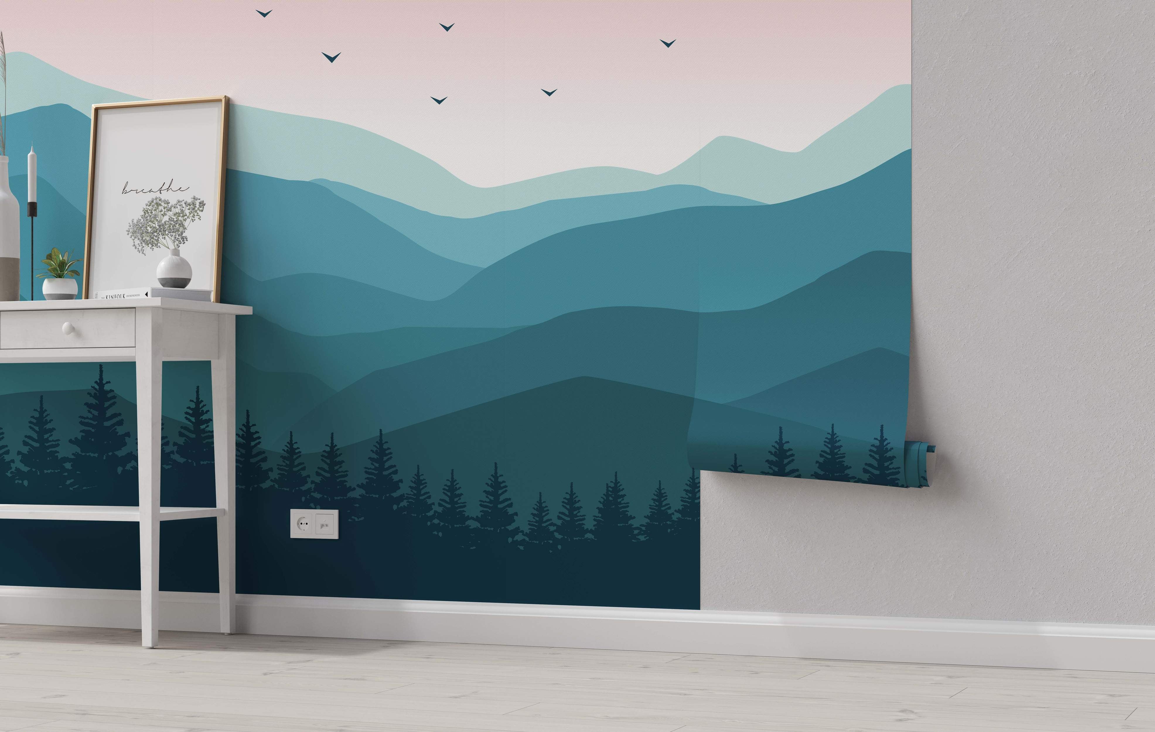 Minimalist landscape mural featuring layered teal and blue mountains, a dark forest silhouette, and a pale pink sky with bird silhouettes.