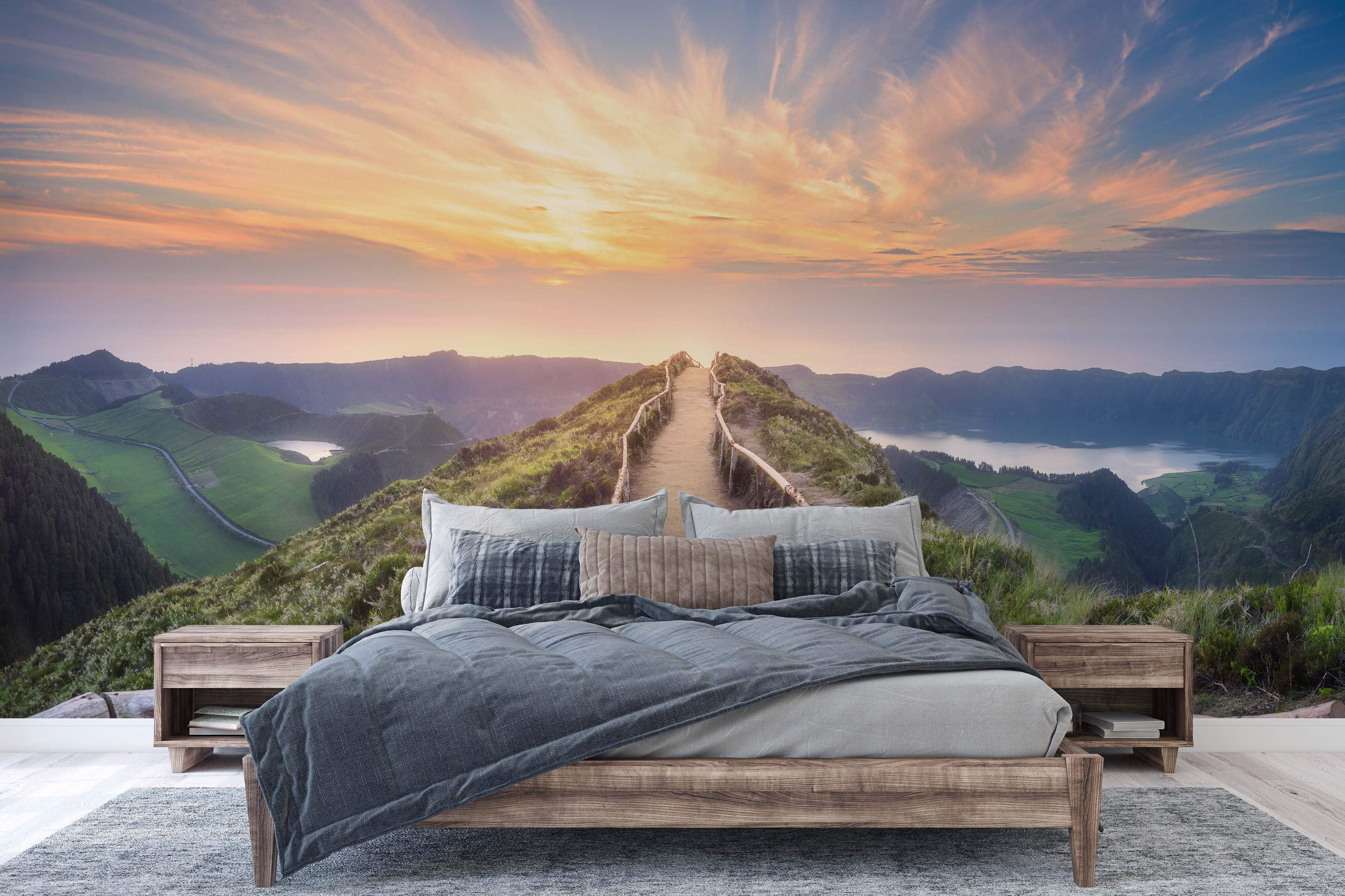 Scenic landscape mural depicting a dirt path on a mountain ridge at sunset, overlooking green valleys and lakes under an orange and blue sky.