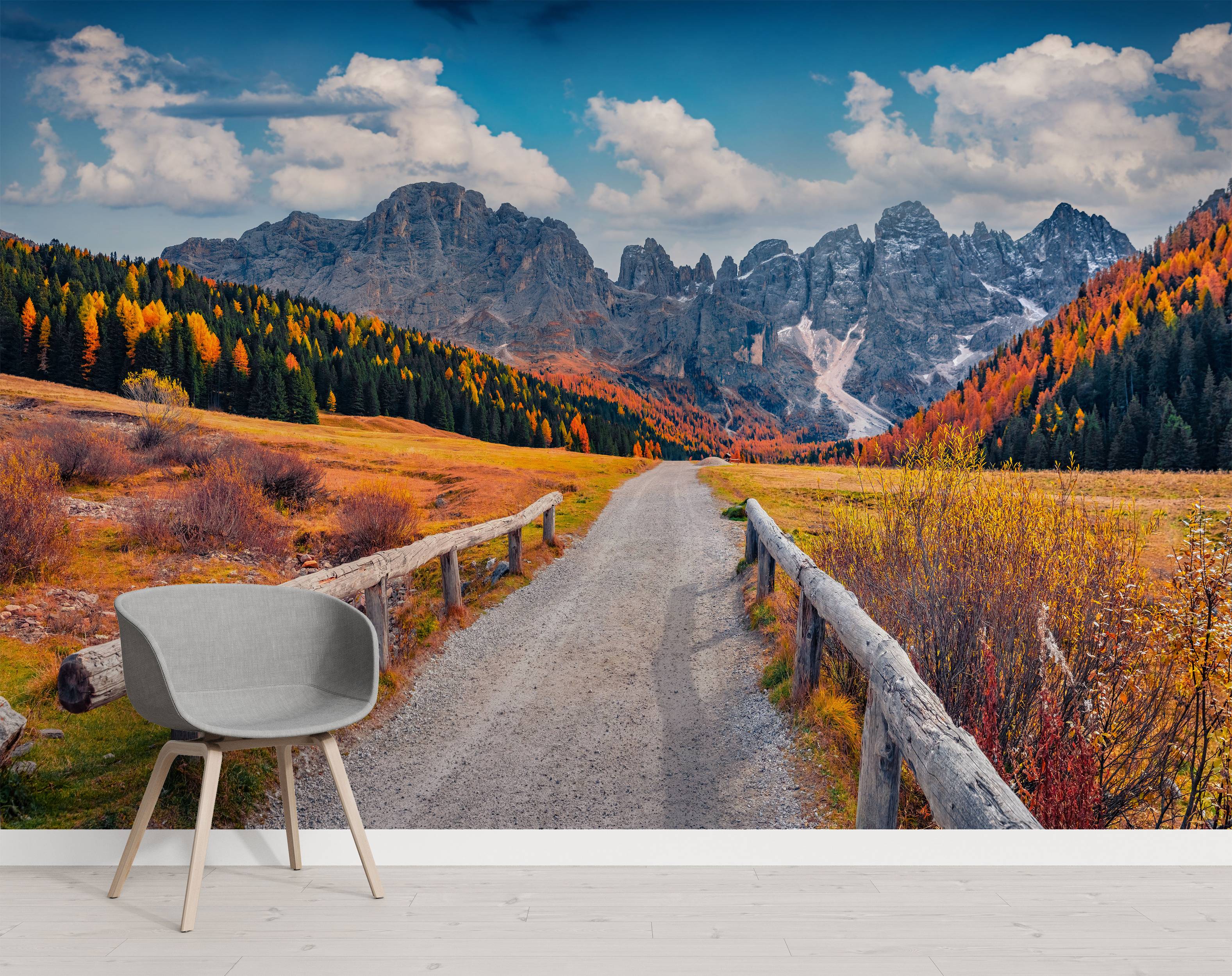 A photorealistic mural of an autumn mountain landscape. A gravel road winds through a valley of golden trees towards gray, snowy peaks.