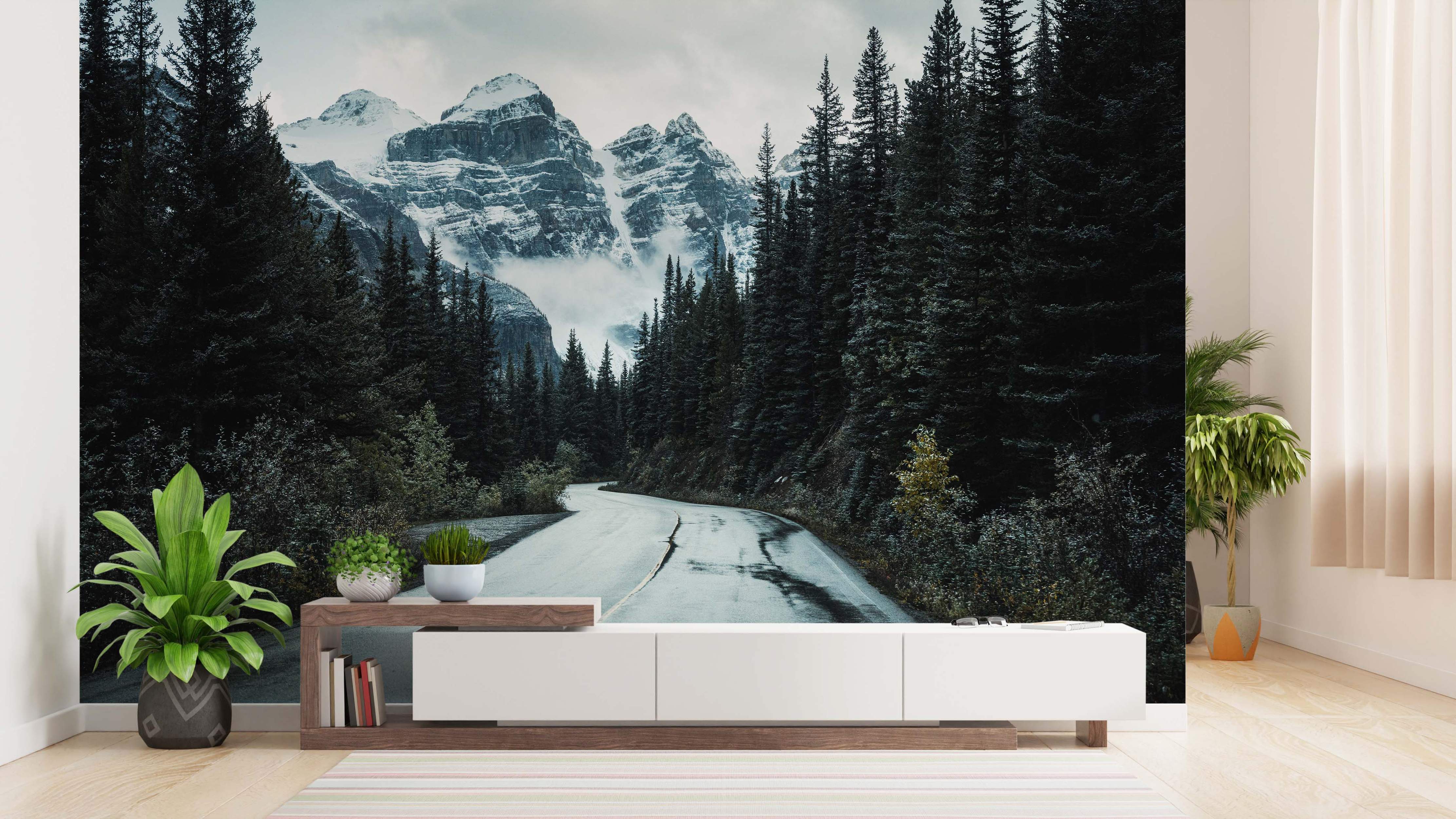 Mural depicting a winding road through a dark pine forest leading towards snow-capped mountains under a cloudy sky.