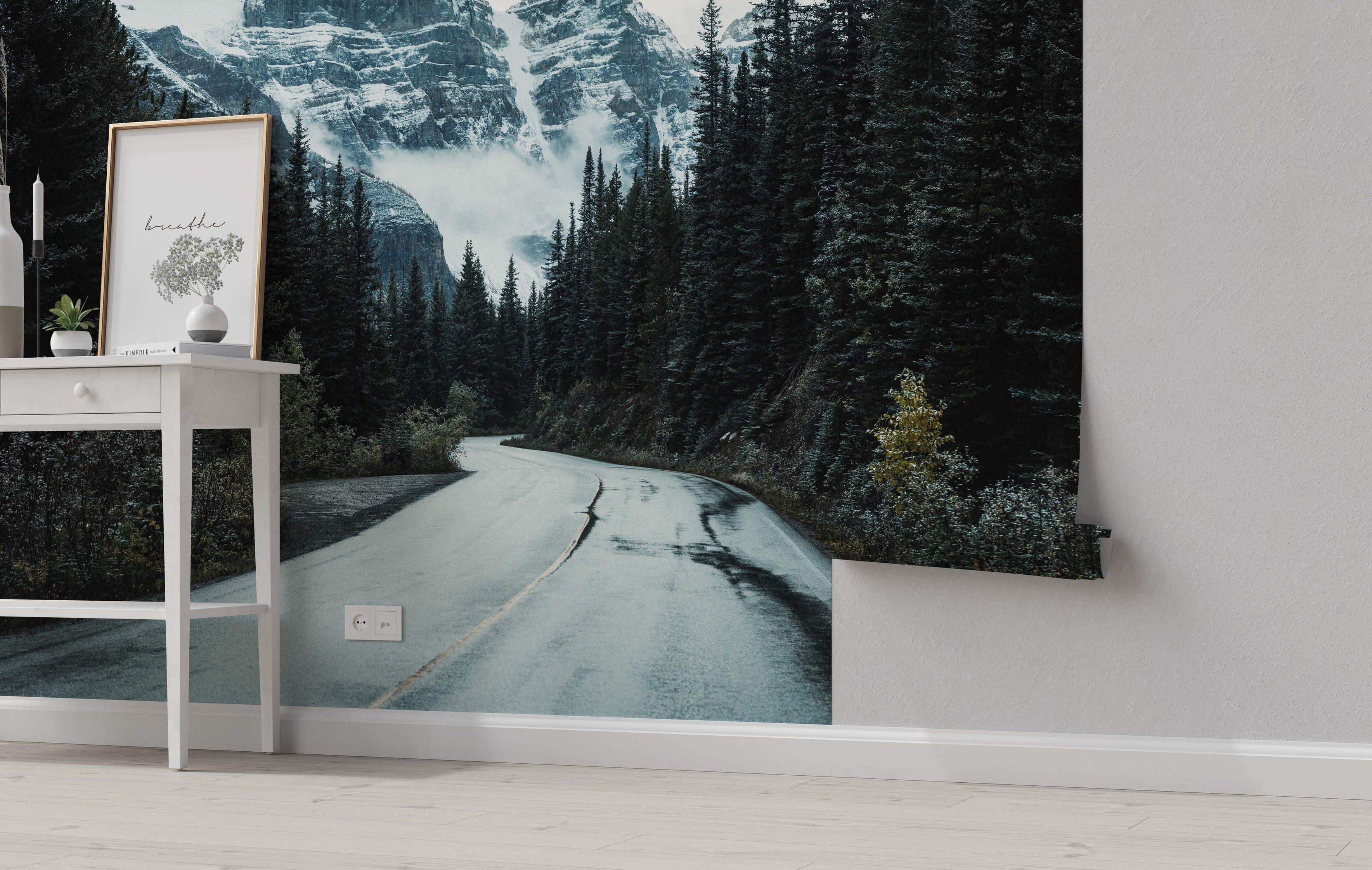 Scenic mural featuring a winding road through a dark green forest towards snow-capped mountains under misty skies.