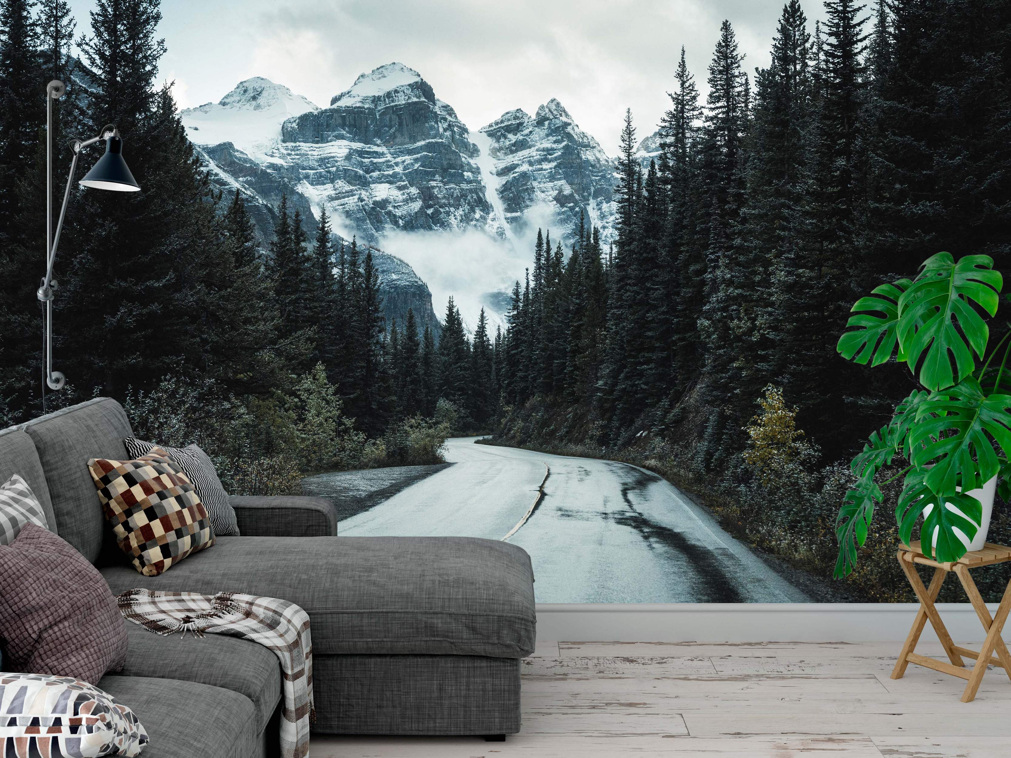 Photorealistic mural of a winding wet road through a pine forest leading towards dramatic snow-capped mountains under a cloudy sky.