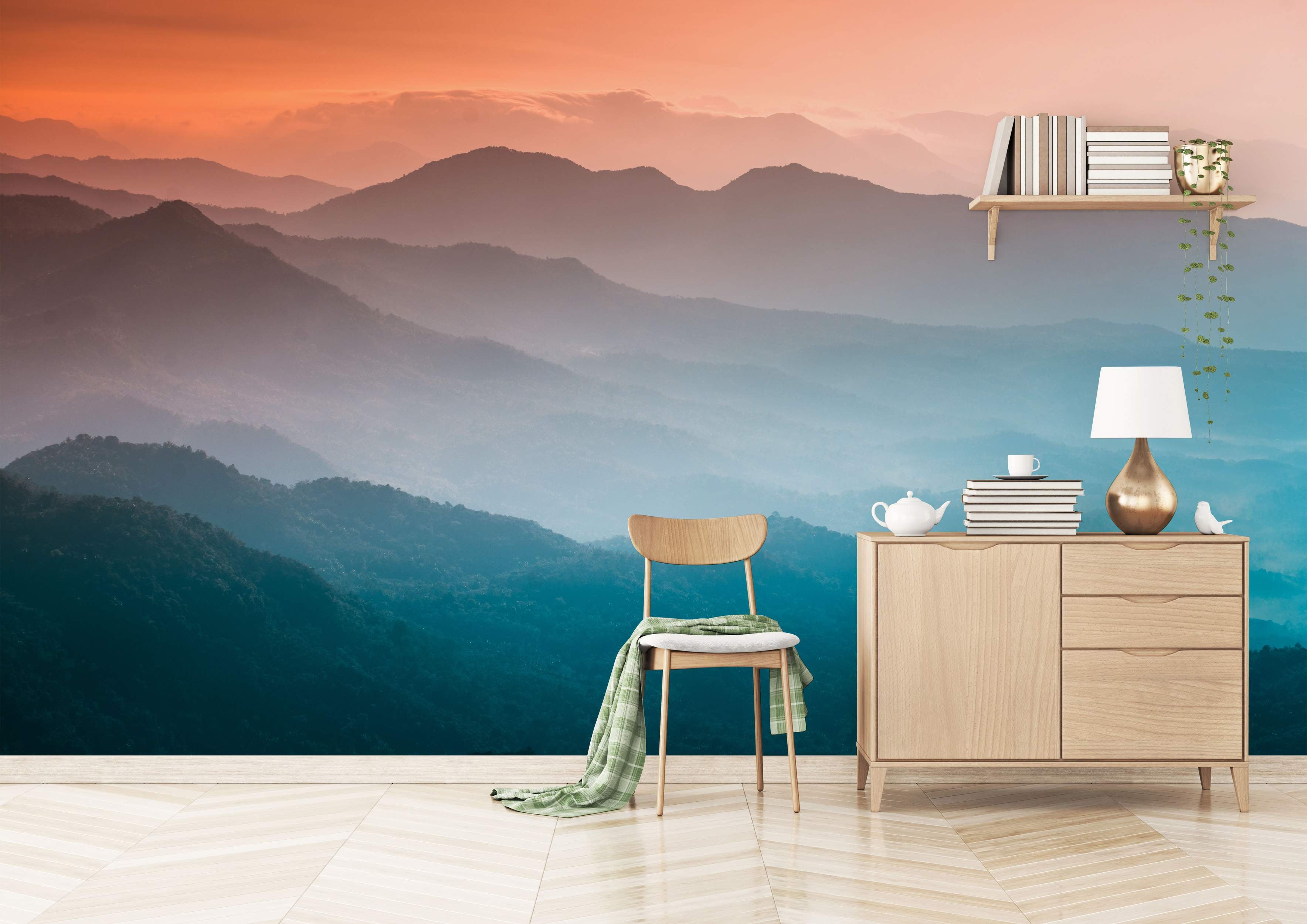 A scenic mural depicting layers of misty mountains under an orange and blue gradient sunset sky.