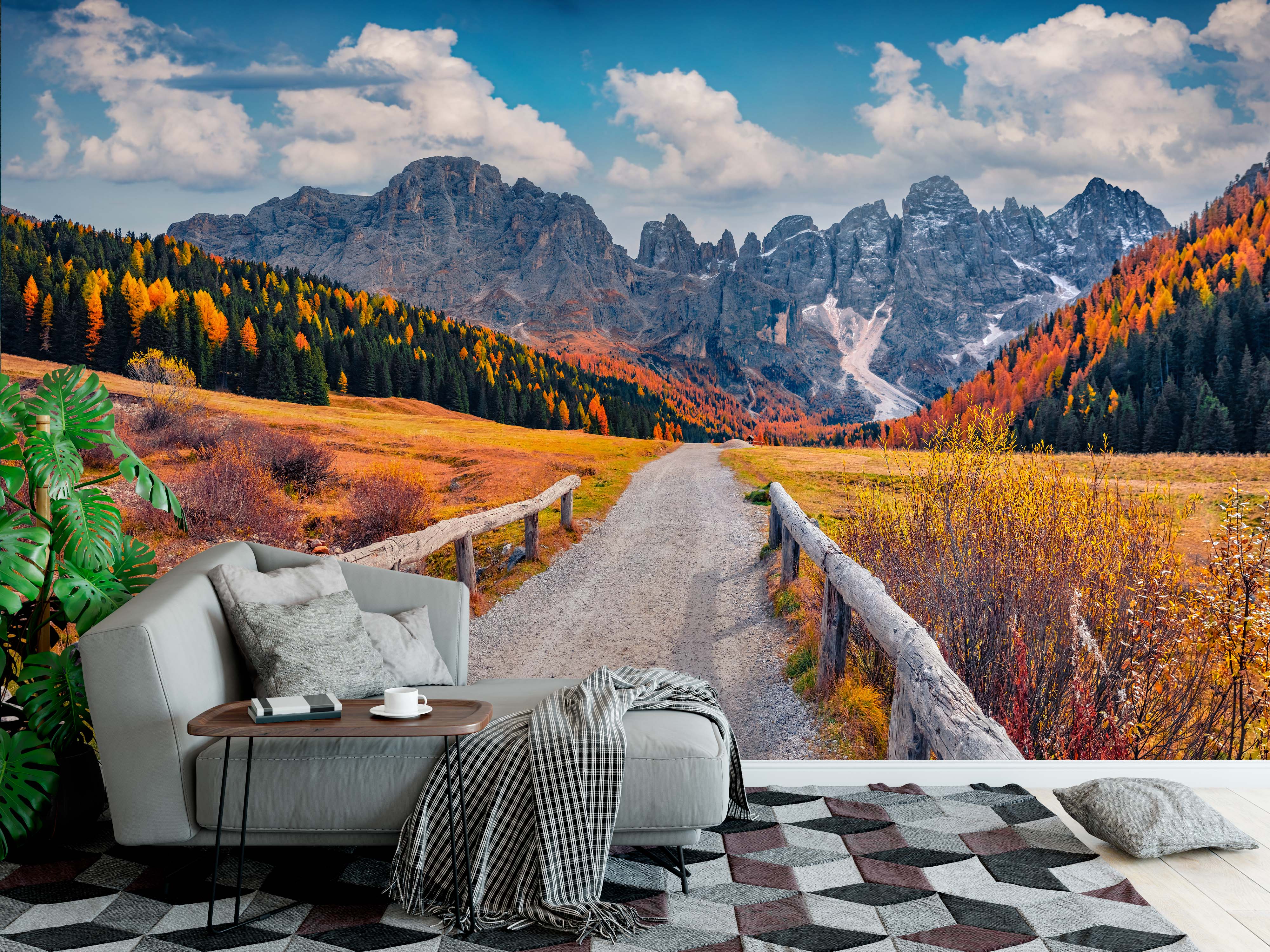 A scenic wall mural of a dirt road through an autumn mountain valley with orange and yellow trees under a cloudy blue sky.