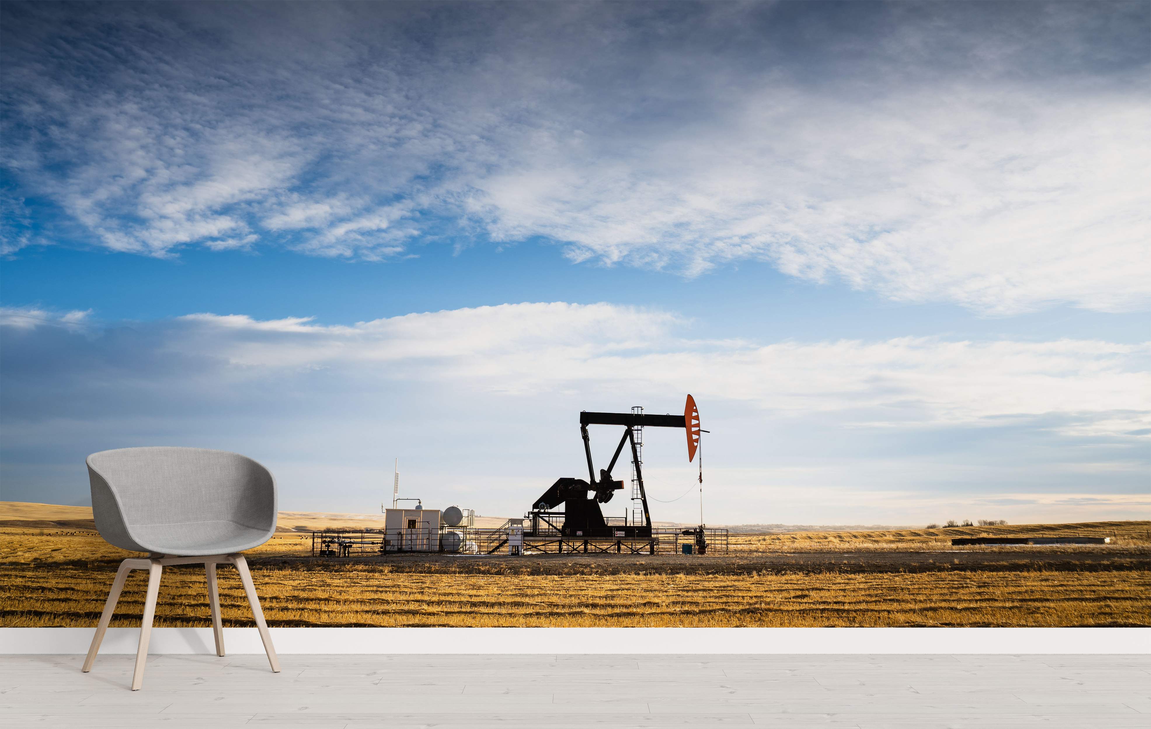 Photographic mural of an oil pumpjack silhouetted against a vast blue sky with clouds, set in a golden-brown field.