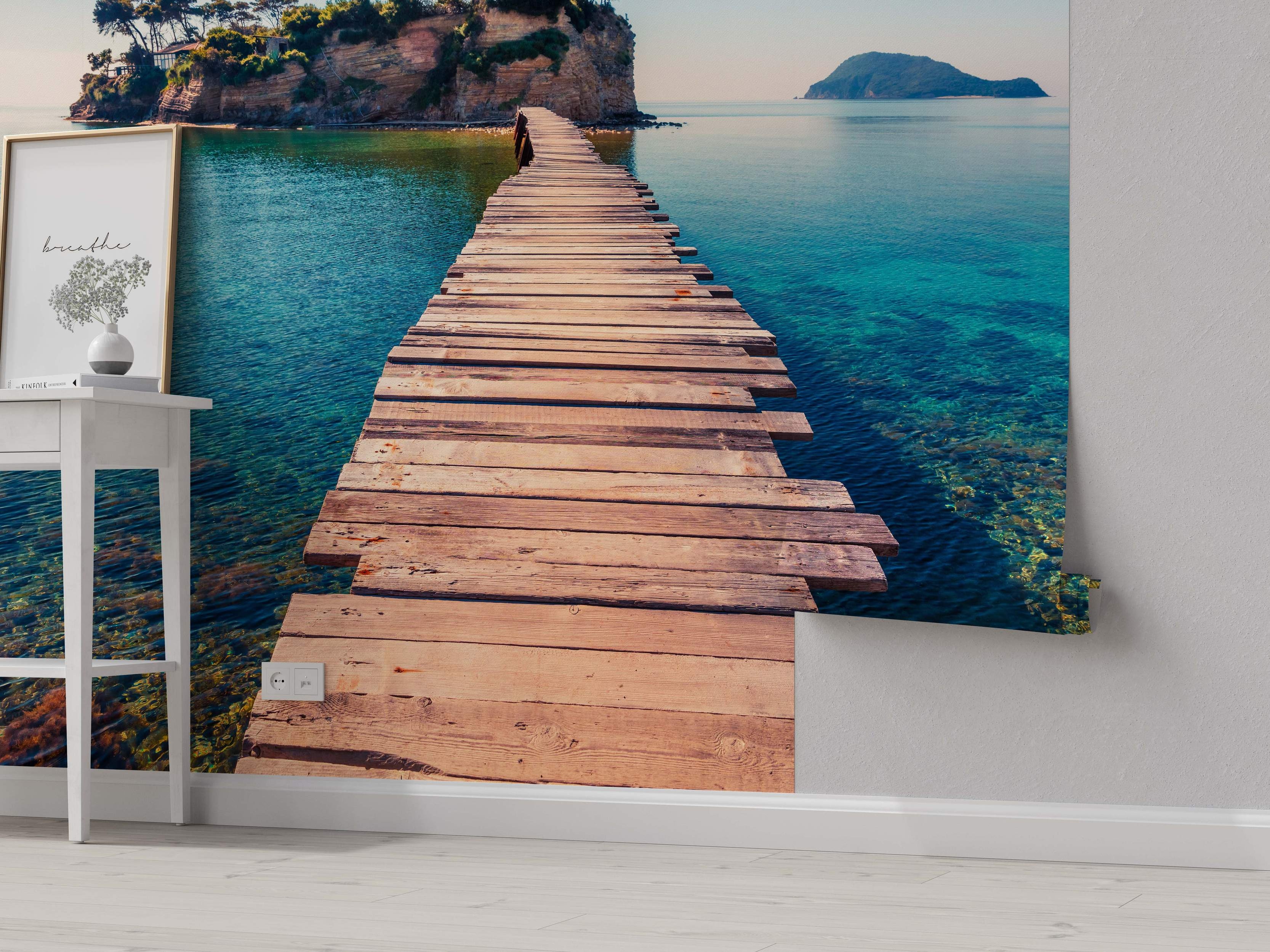 Scenic mural depicting a rustic wooden pier extending over clear turquoise water towards a rocky island with trees.