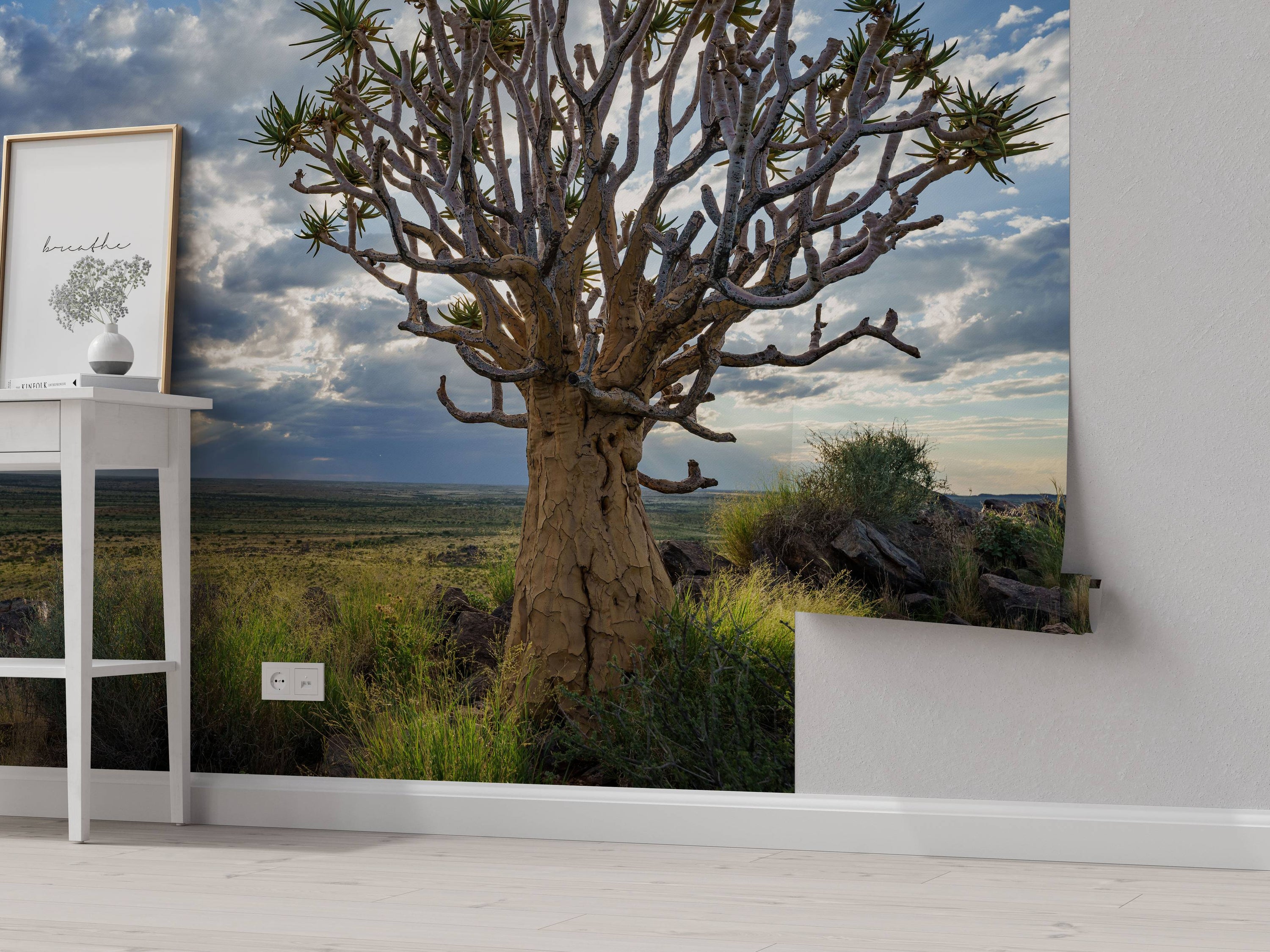 A photorealistic mural of a large quiver tree in a grassy savanna landscape under a dramatic, cloudy sky.
