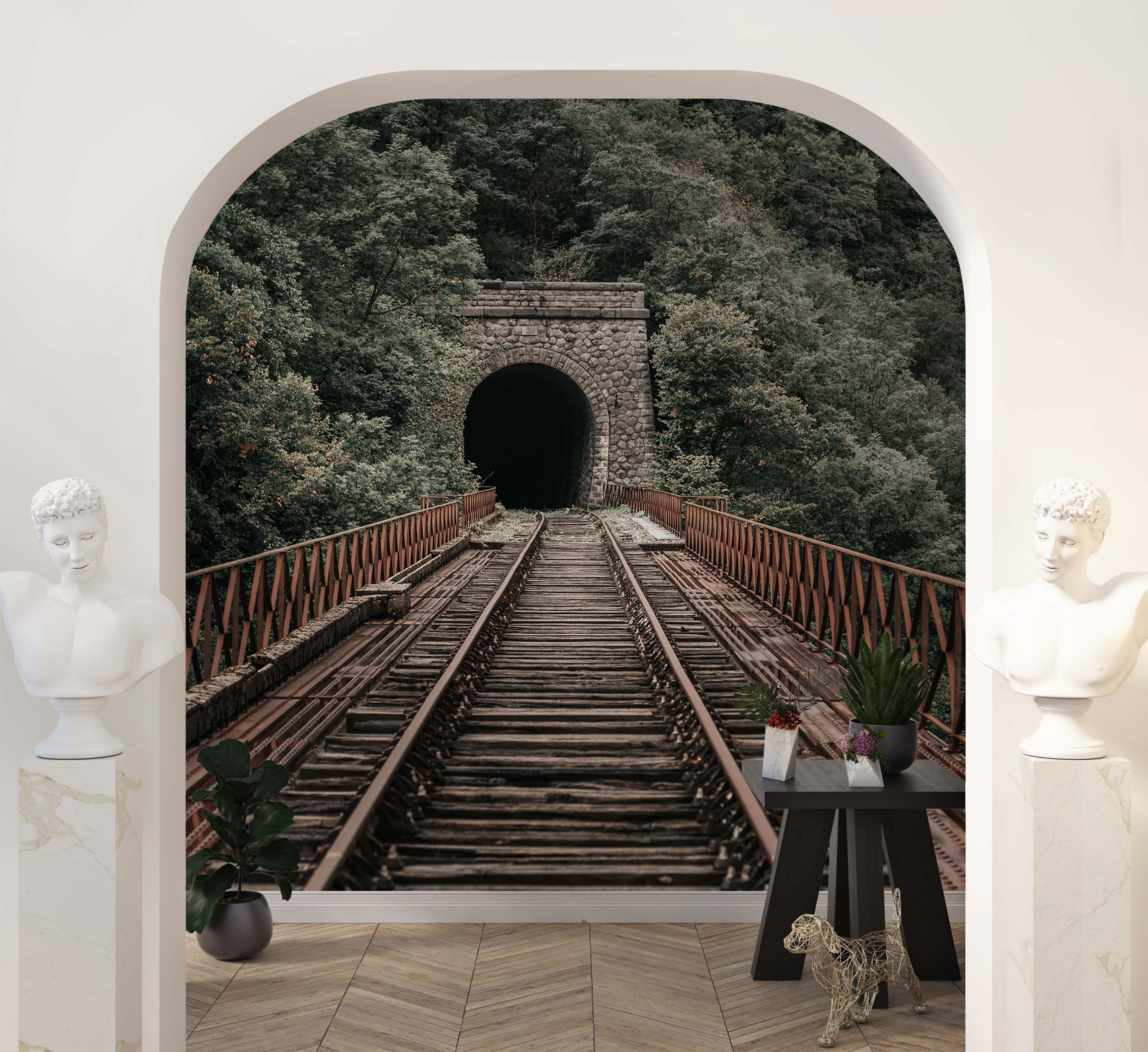 A photorealistic mural of old railway tracks on a bridge leading into a dark stone tunnel surrounded by a dense green forest.