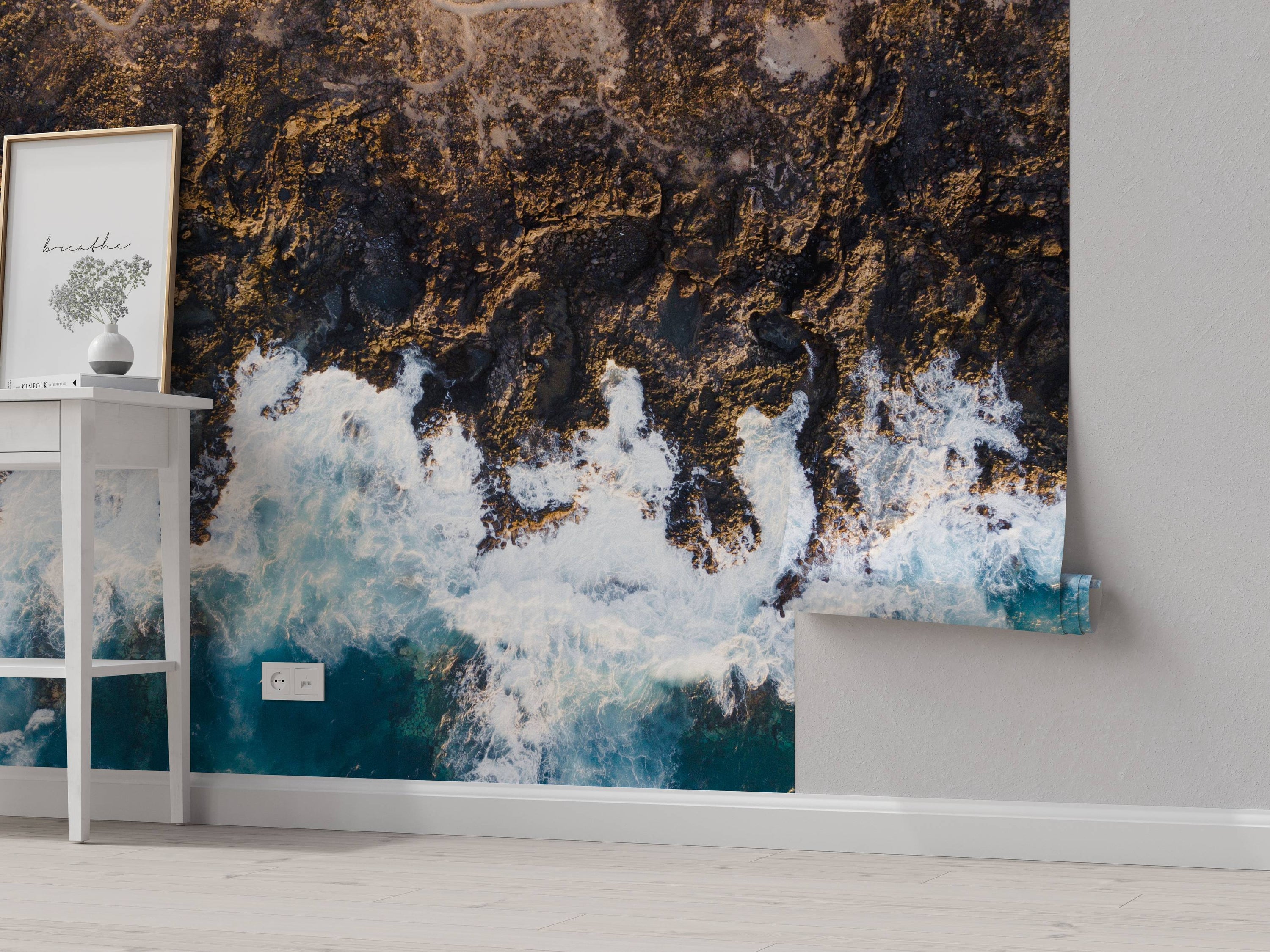 An aerial view mural of a rugged, rocky coastline with white ocean waves crashing against the dark shore.