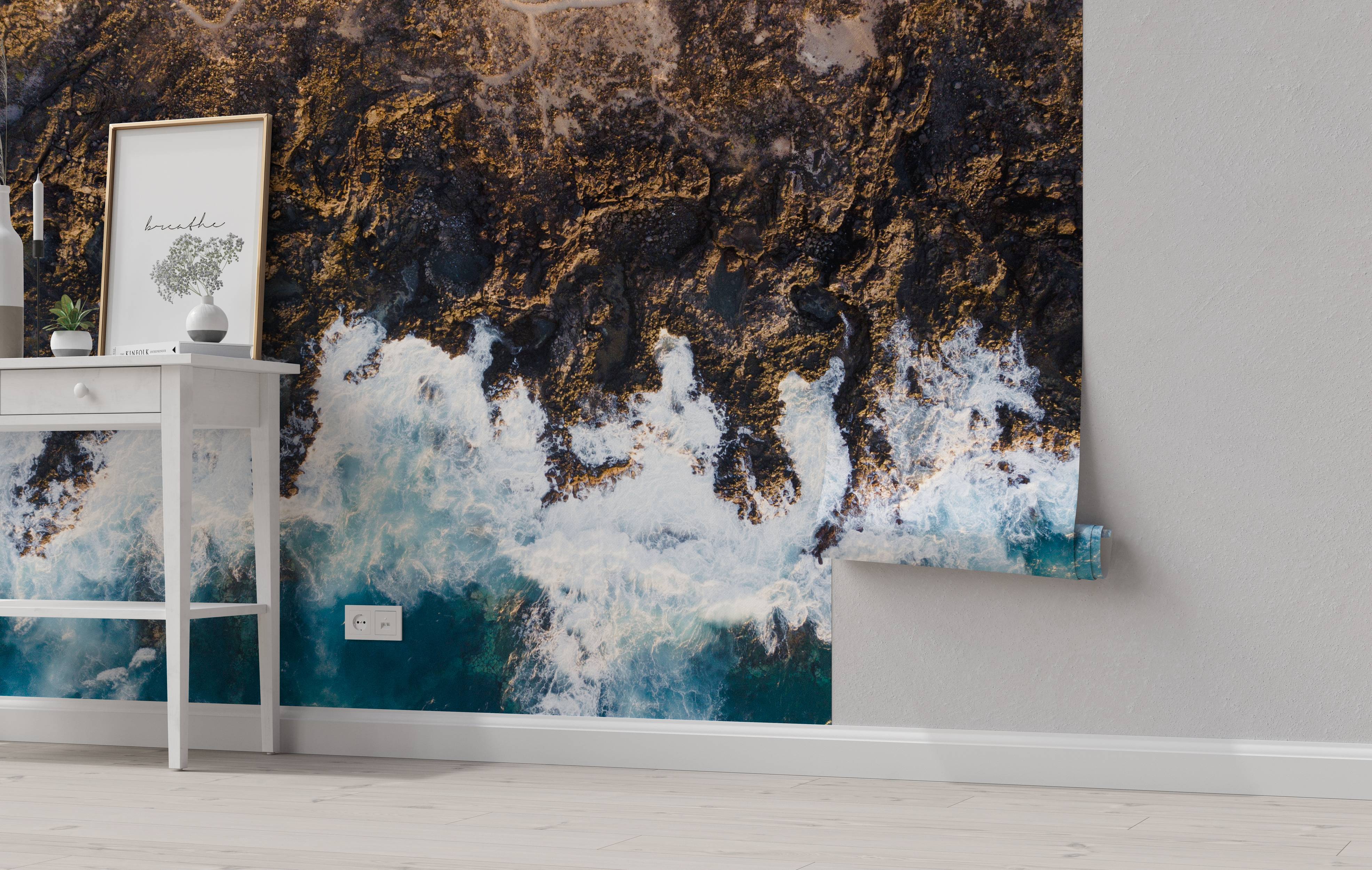 An aerial view mural of a rugged, rocky coastline with white ocean waves crashing against the dark shore.