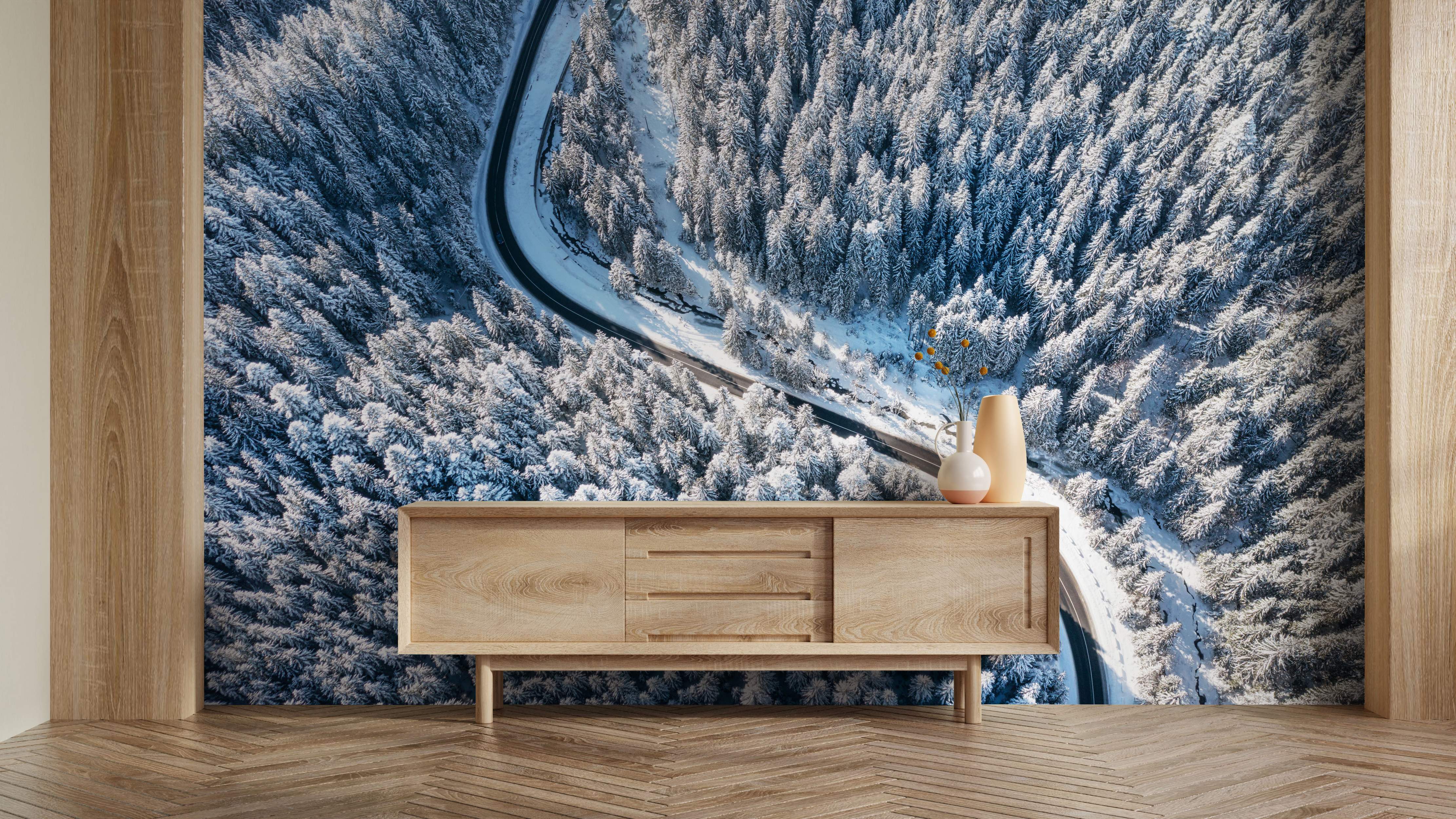 Aerial view mural depicting a winding road cutting through a vast, snow-blanketed evergreen forest.