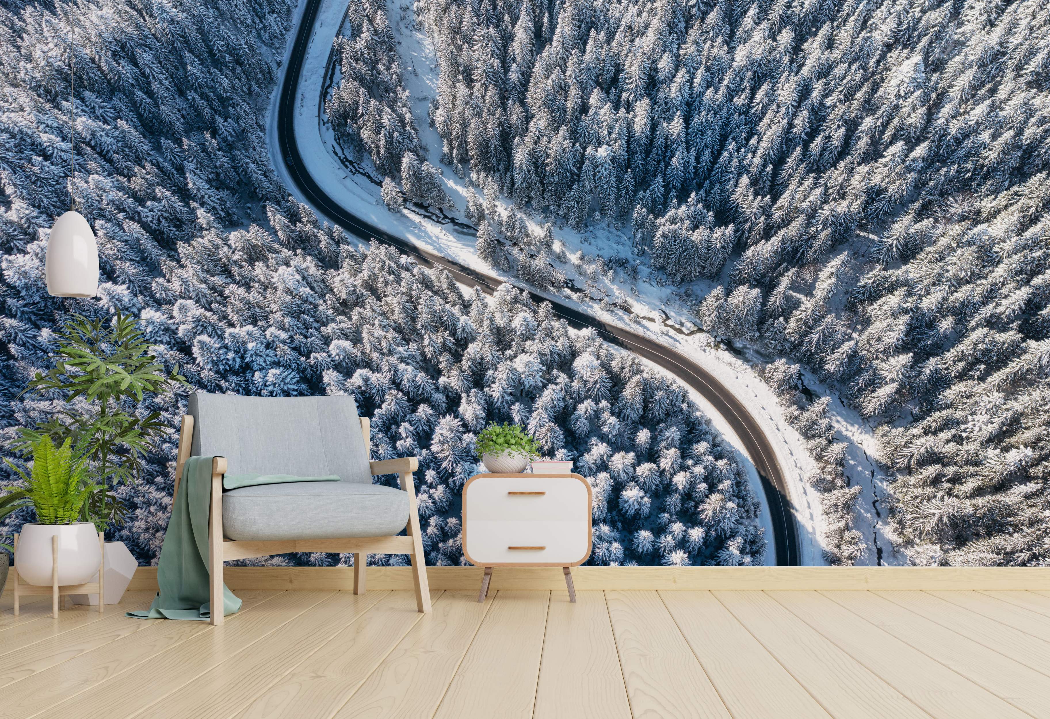 Aerial view mural depicting a winding road through a dense, snow-covered pine forest in winter.