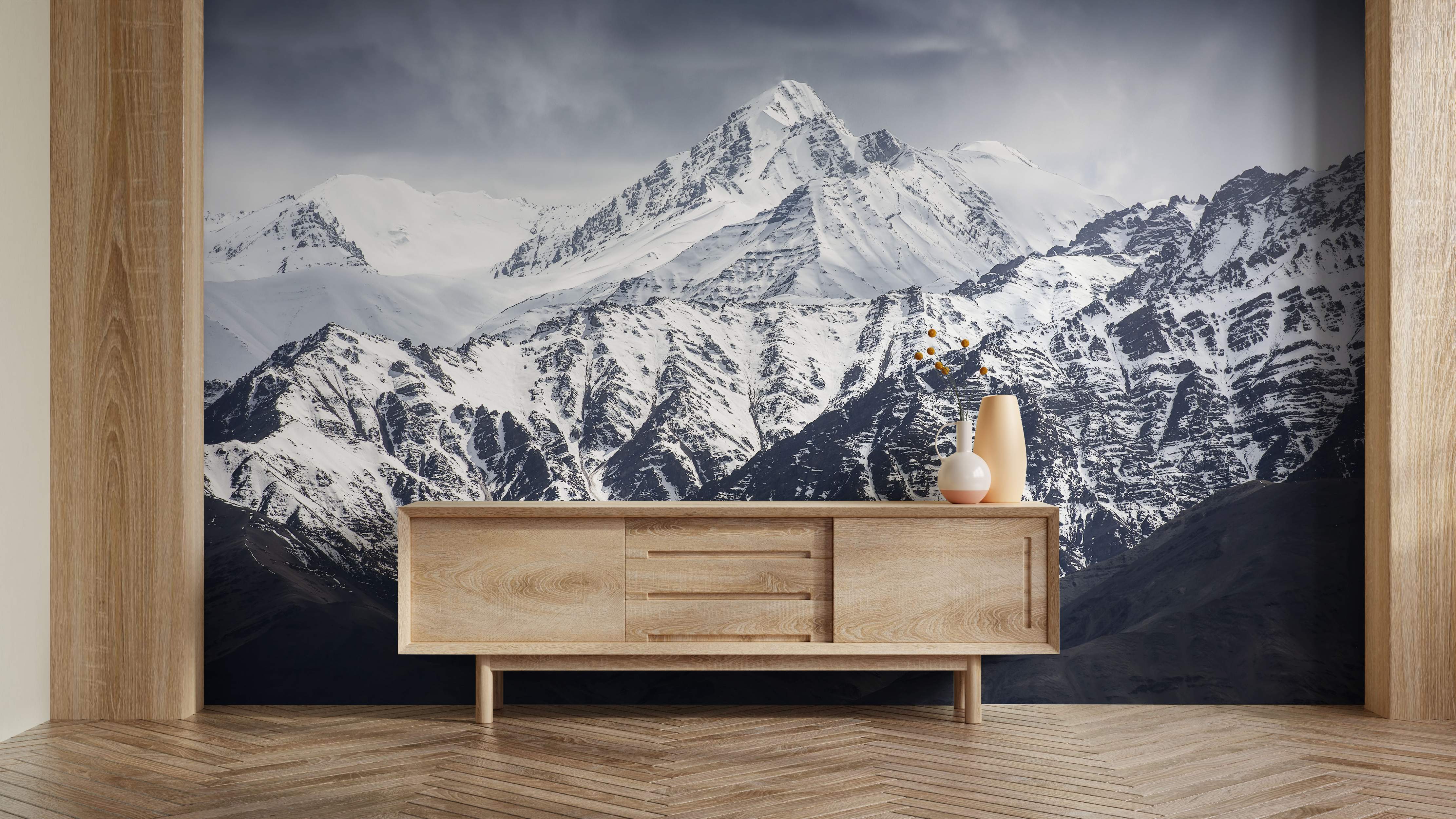 Photorealistic wall mural featuring a majestic snow-covered mountain range with steep, rocky slopes under a moody gray sky.