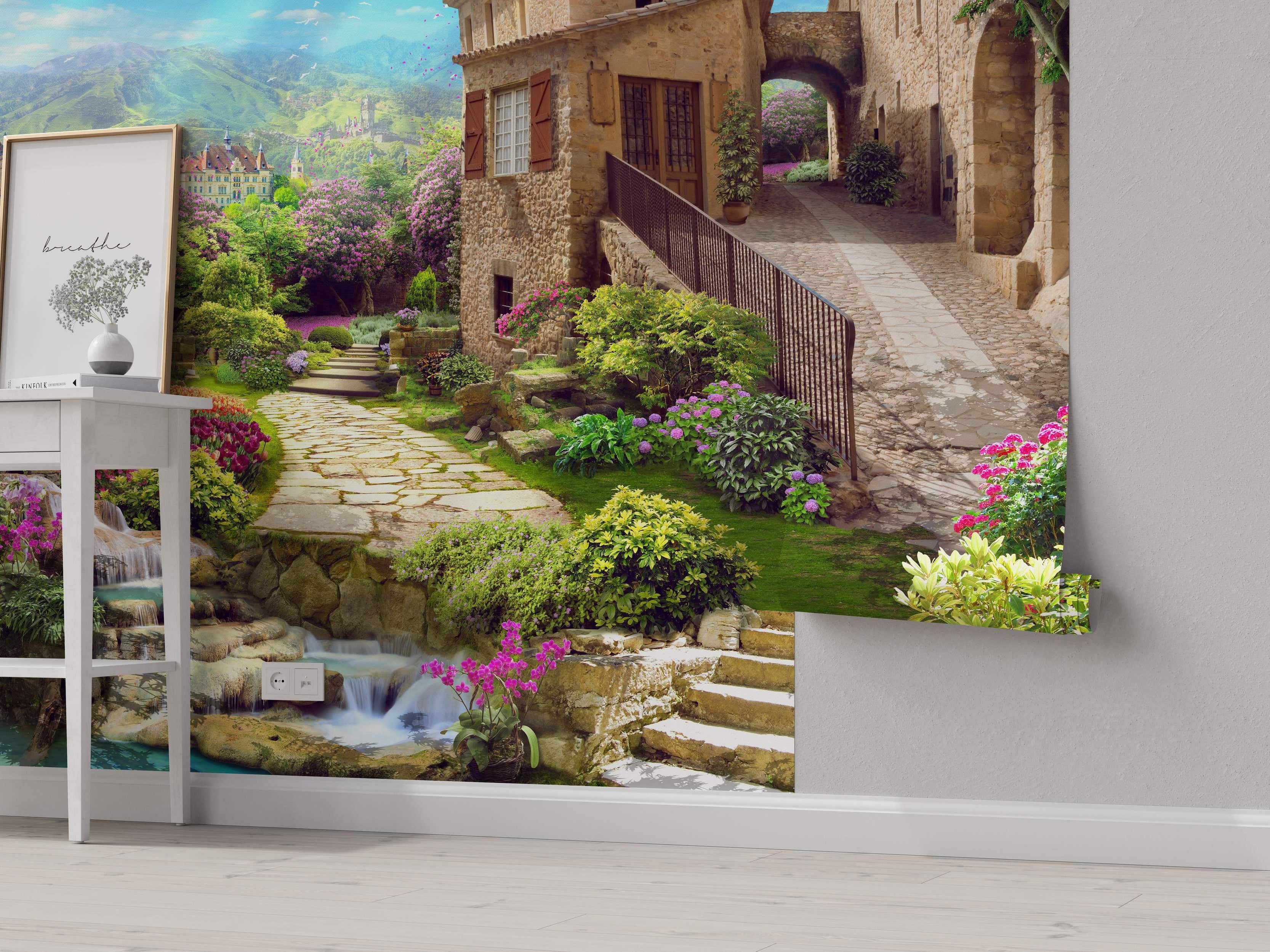 Mural depicting a charming European stone village street with gardens, flowers, a waterfall, and mountain scenery.