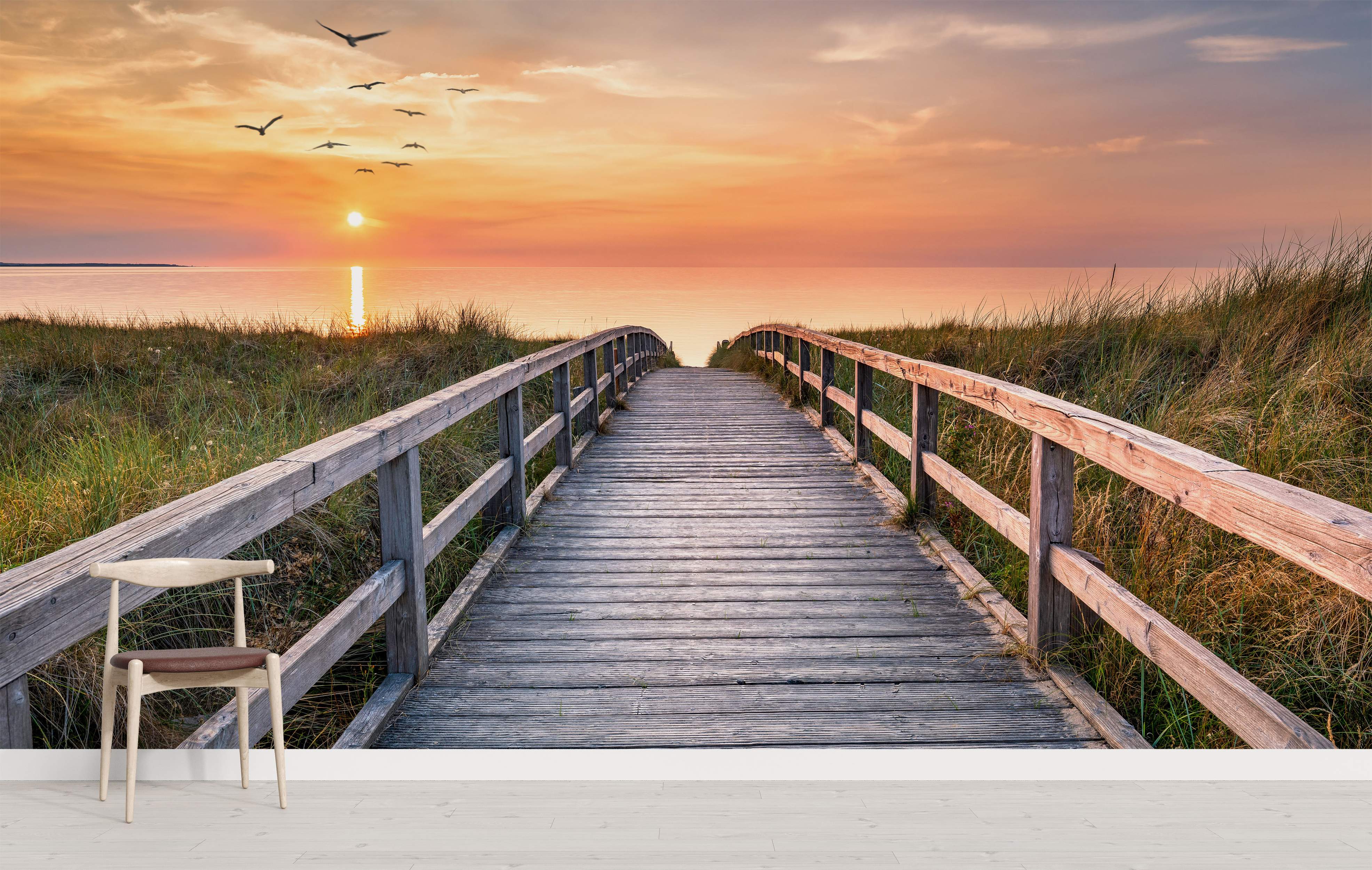 Mural featuring a wooden boardwalk through grassy dunes leading to the ocean under a vibrant orange sunset sky with birds.