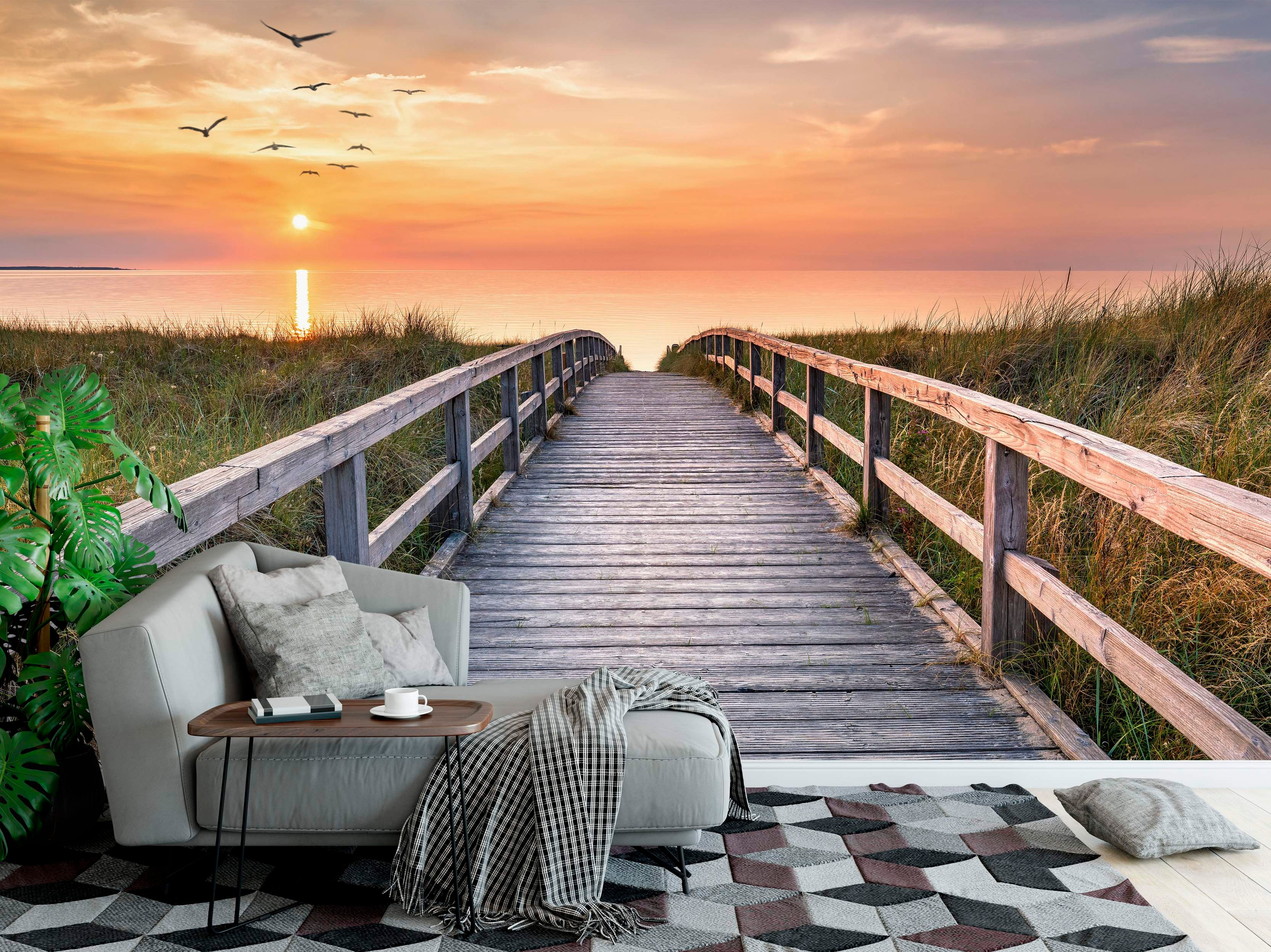 Mural depicting a wooden boardwalk leading through grassy dunes towards an orange sunset over the ocean with birds flying.