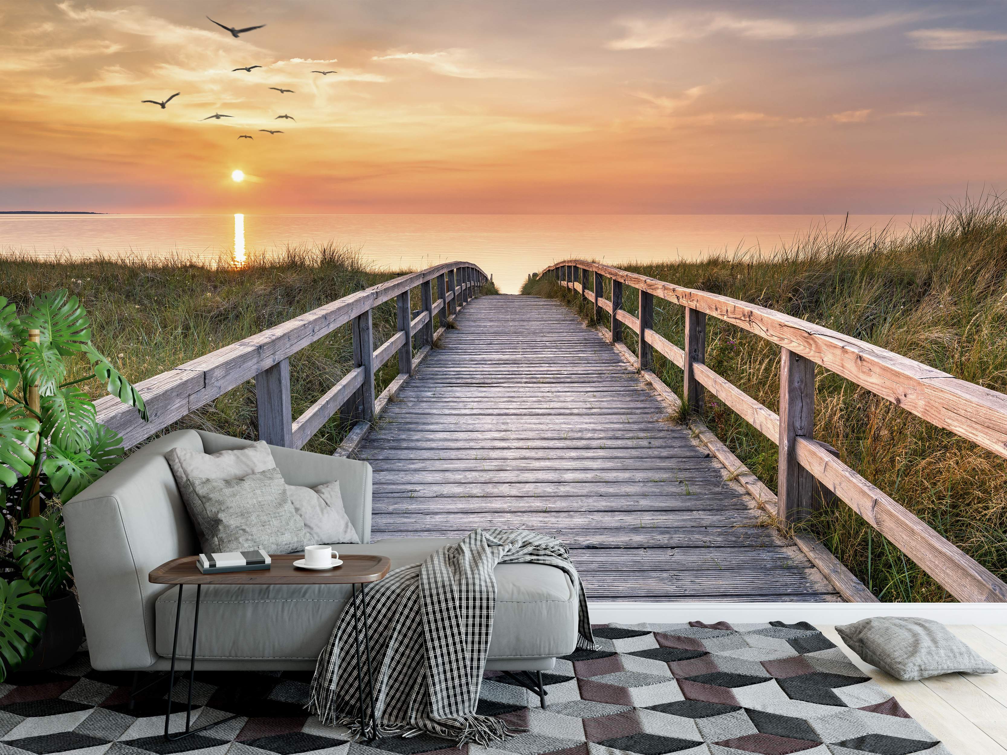Mural depicting a wooden boardwalk leading through grassy dunes towards an orange sunset over the ocean with birds flying.