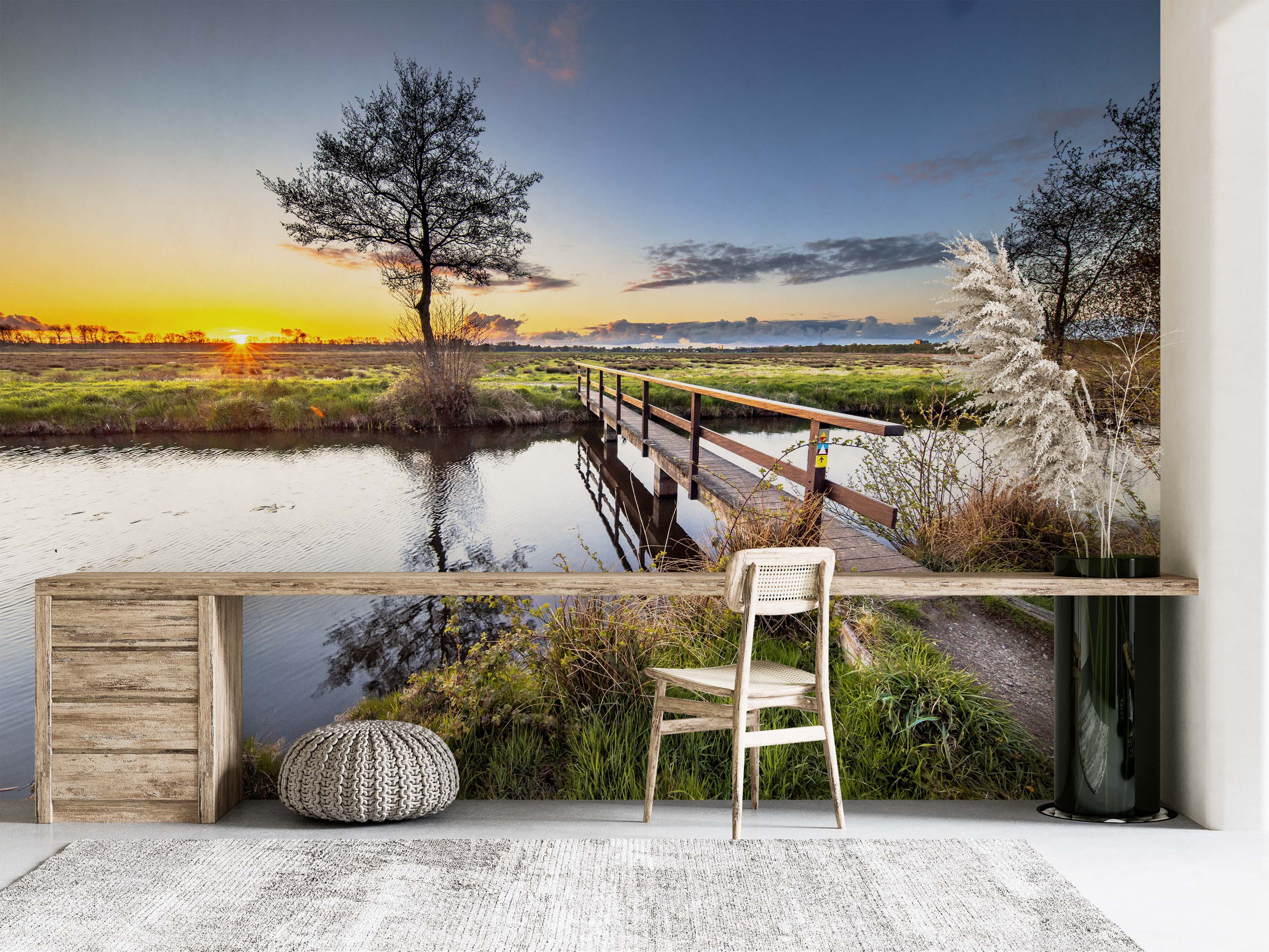 A photorealistic mural of a tranquil sunset over a river. A wooden bridge crosses the water, with grassy banks and trees.