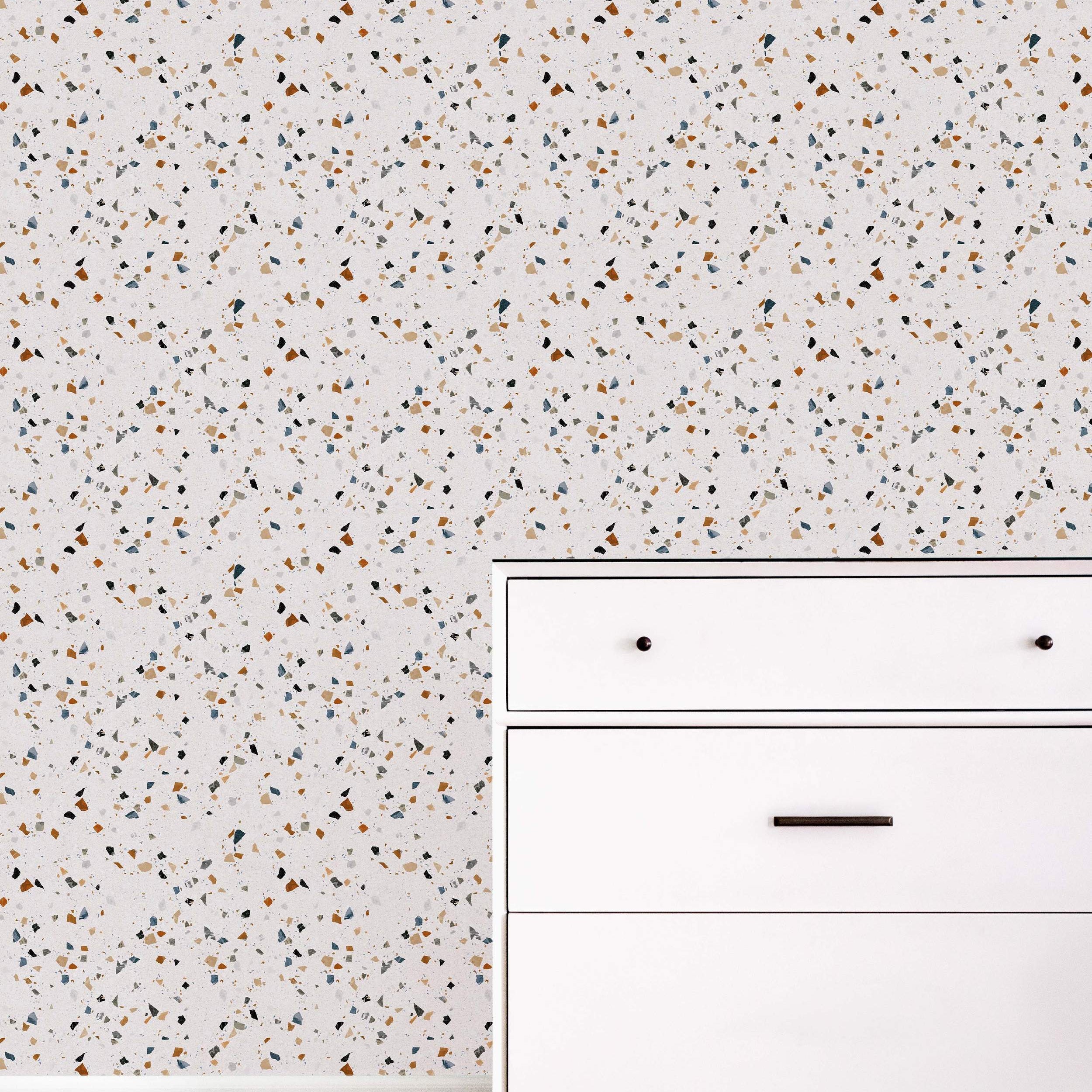 Off-white wallpaper featuring a classic terrazzo pattern with scattered chips in brown, blue, black, and beige.