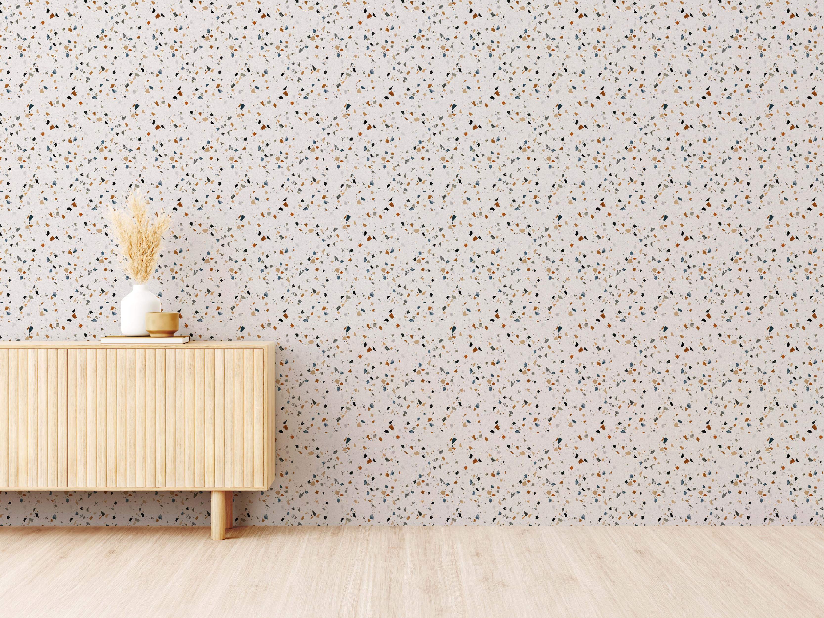 Off-white terrazzo wallpaper with scattered irregular chips in brown, blue, black, and tan tones.