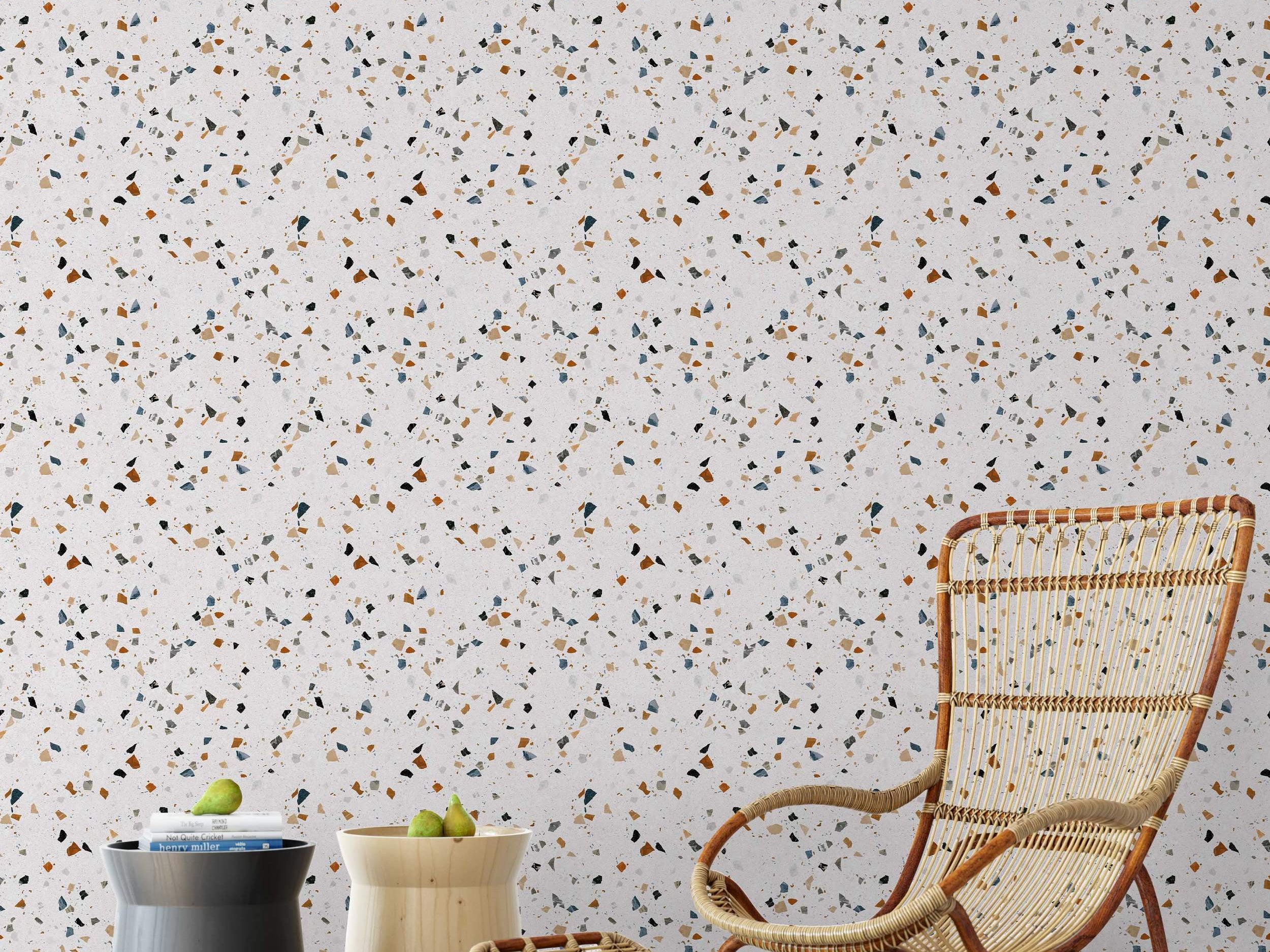 Terrazzo wallpaper featuring scattered, multi-colored chips in brown, blue, grey, and black on a light background.
