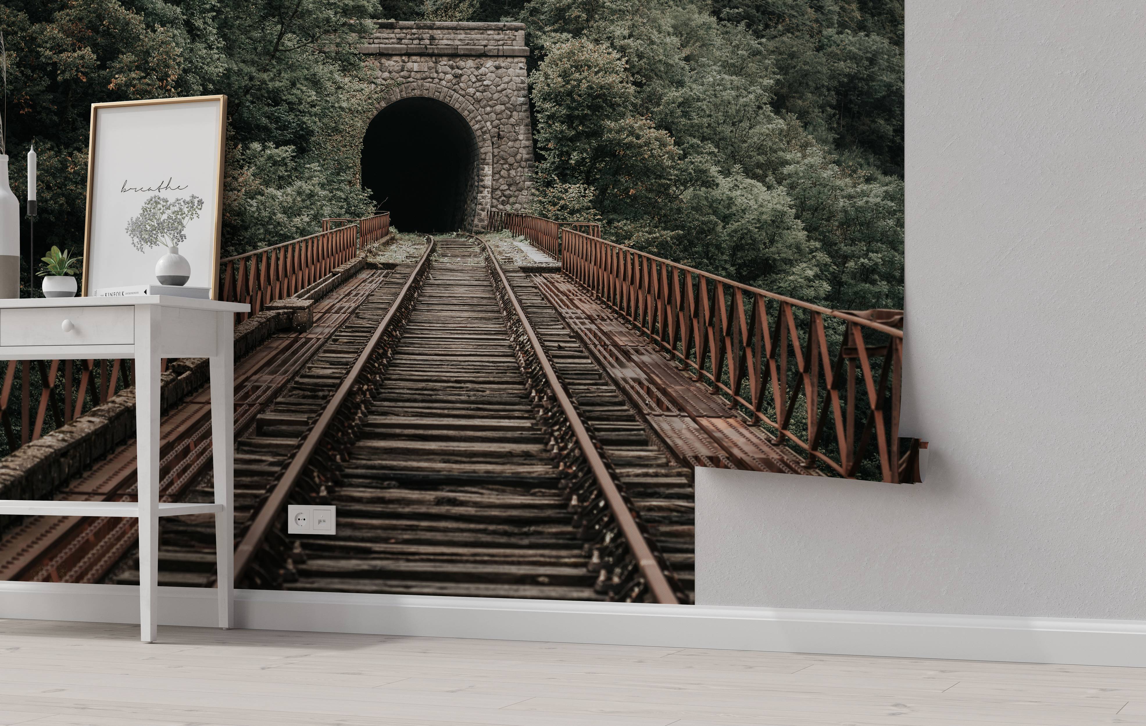 A photorealistic mural of rusty train tracks on a bridge leading into a dark stone tunnel surrounded by a green forest.