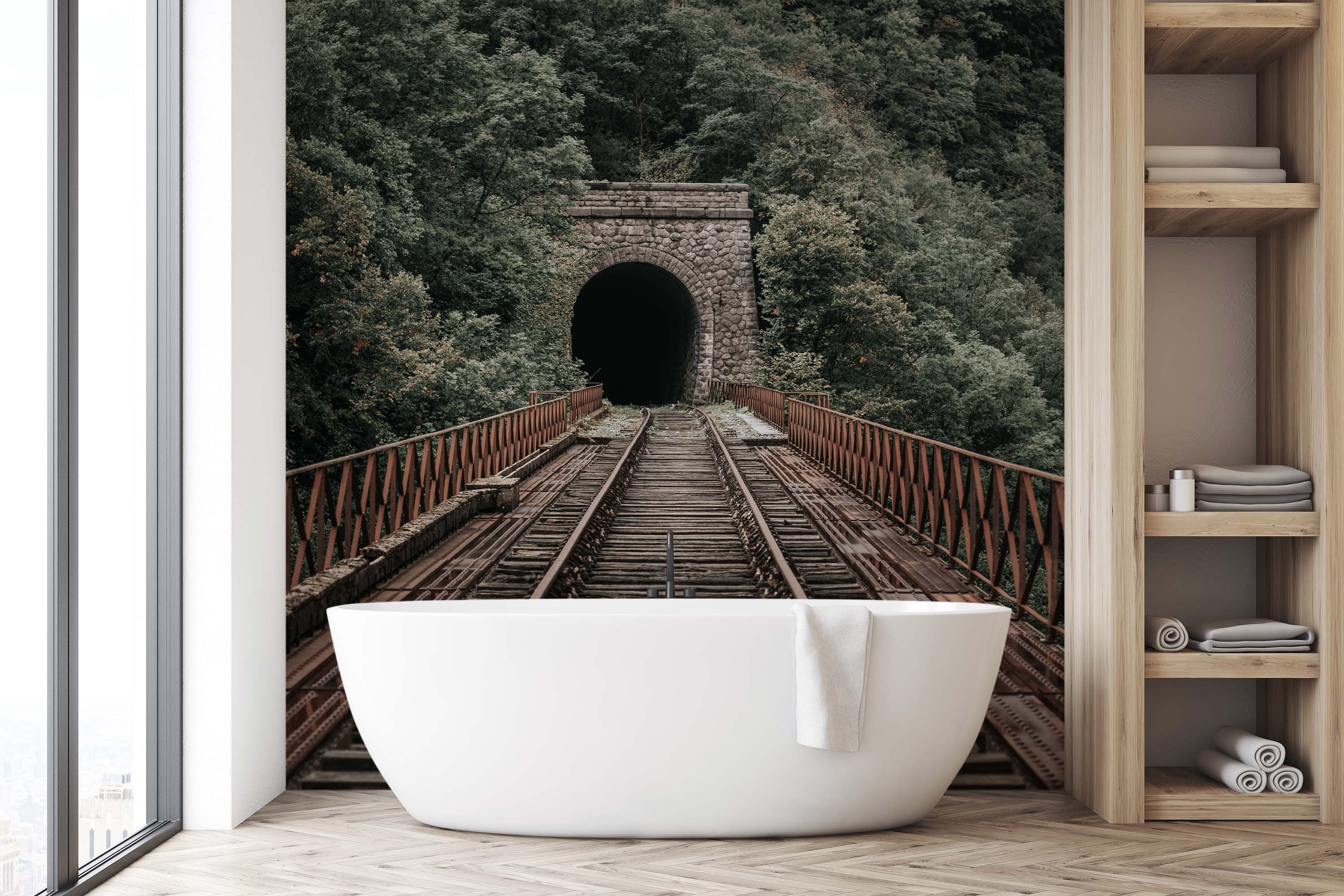 A photorealistic wall mural of rusty train tracks on a bridge leading to a dark stone tunnel in a lush green forest.