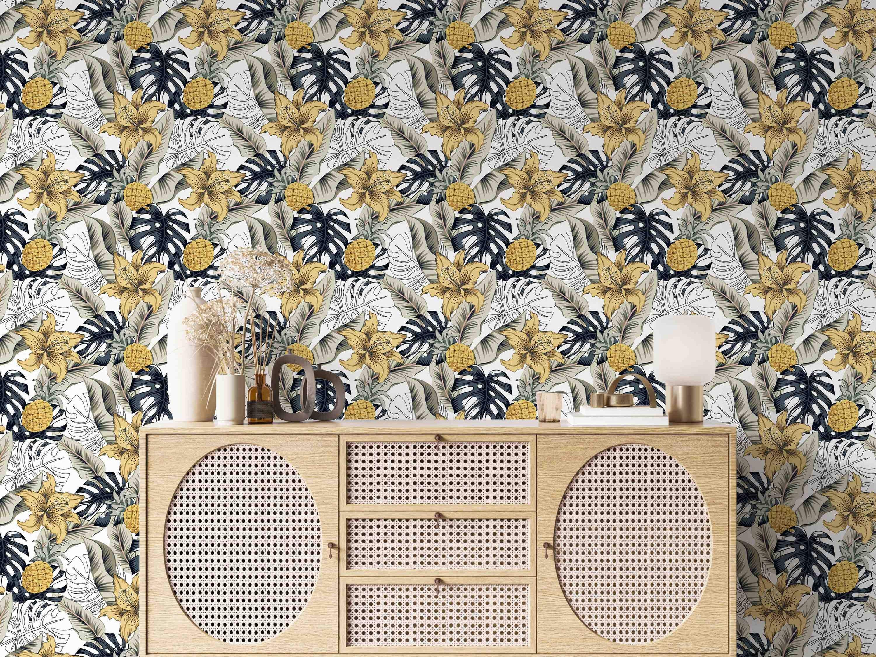 Tropical wallpaper featuring yellow lilies, pineapples, dark blue Monstera, and beige banana leaves on a white background.