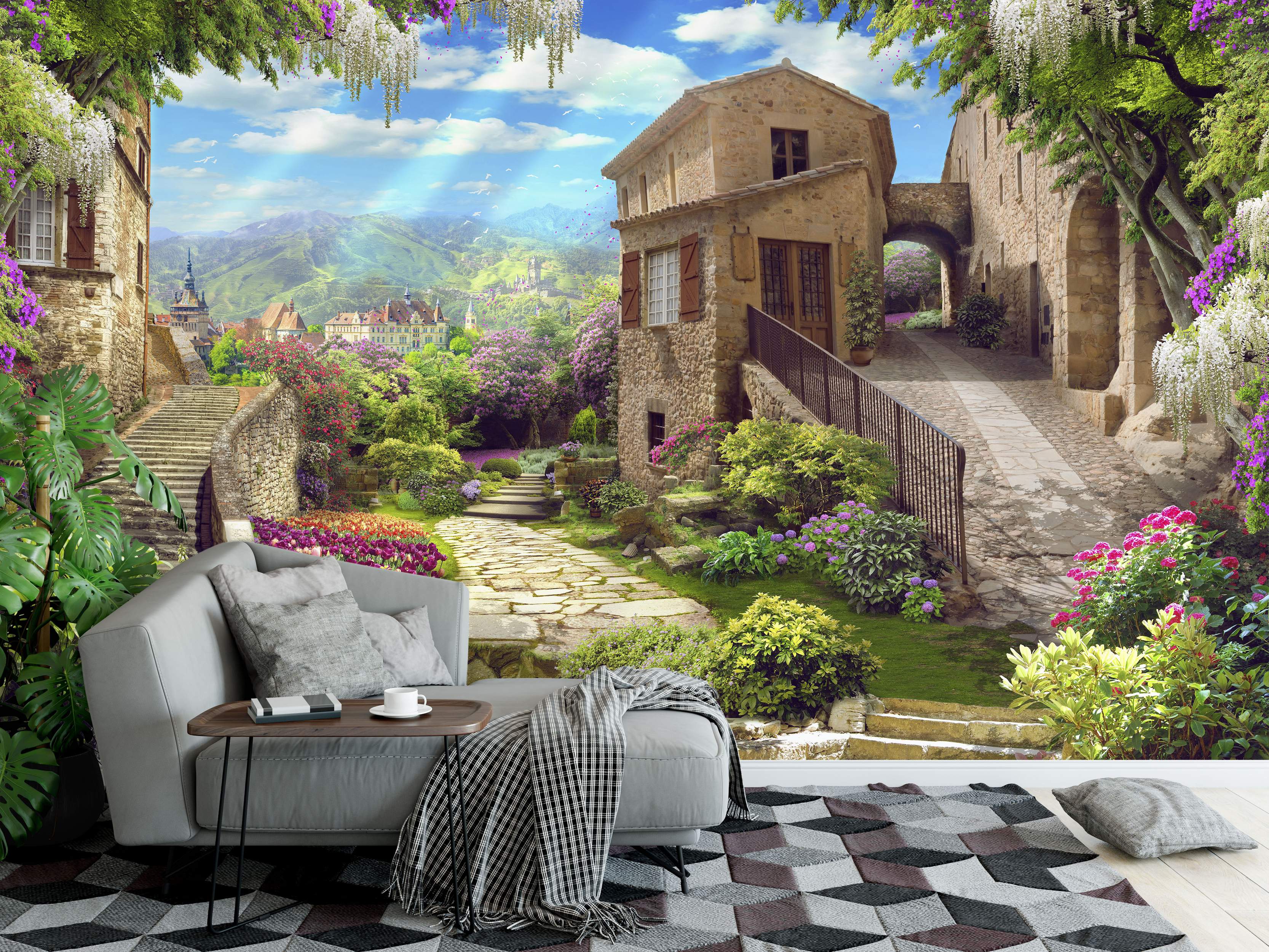 Mural depicting a sunny European village with stone houses, vibrant gardens, wisteria, and mountains under a blue sky.