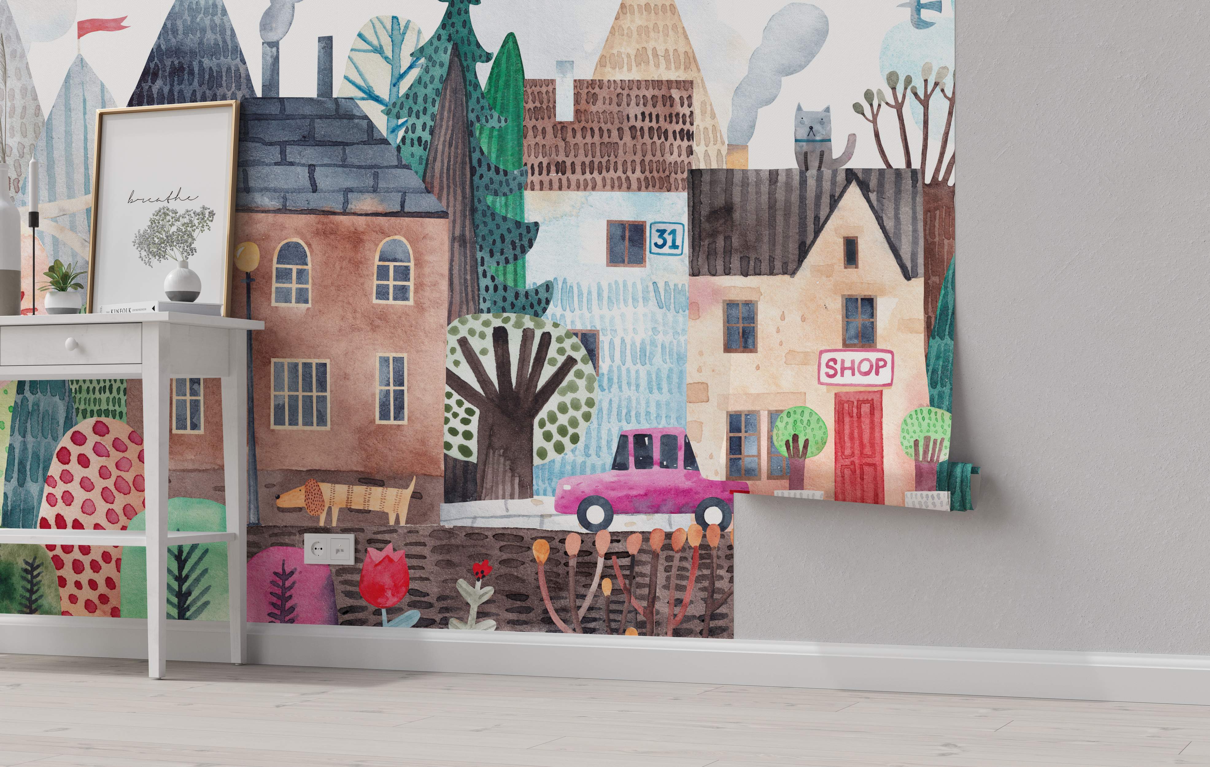 Whimsical watercolor mural depicting a colorful town scene with stylized houses, trees, mountains, a pink car, and a grey cat.