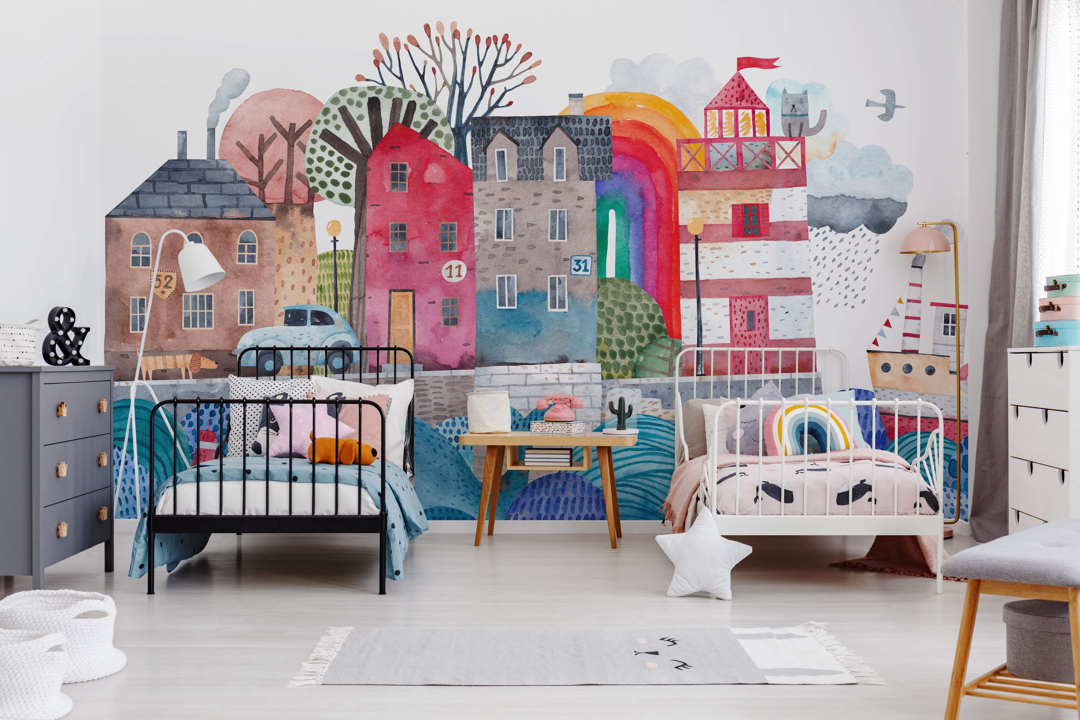 Whimsical watercolor mural featuring a colorful seaside town with stylized houses, a lighthouse, rainbow, ship, and clouds.