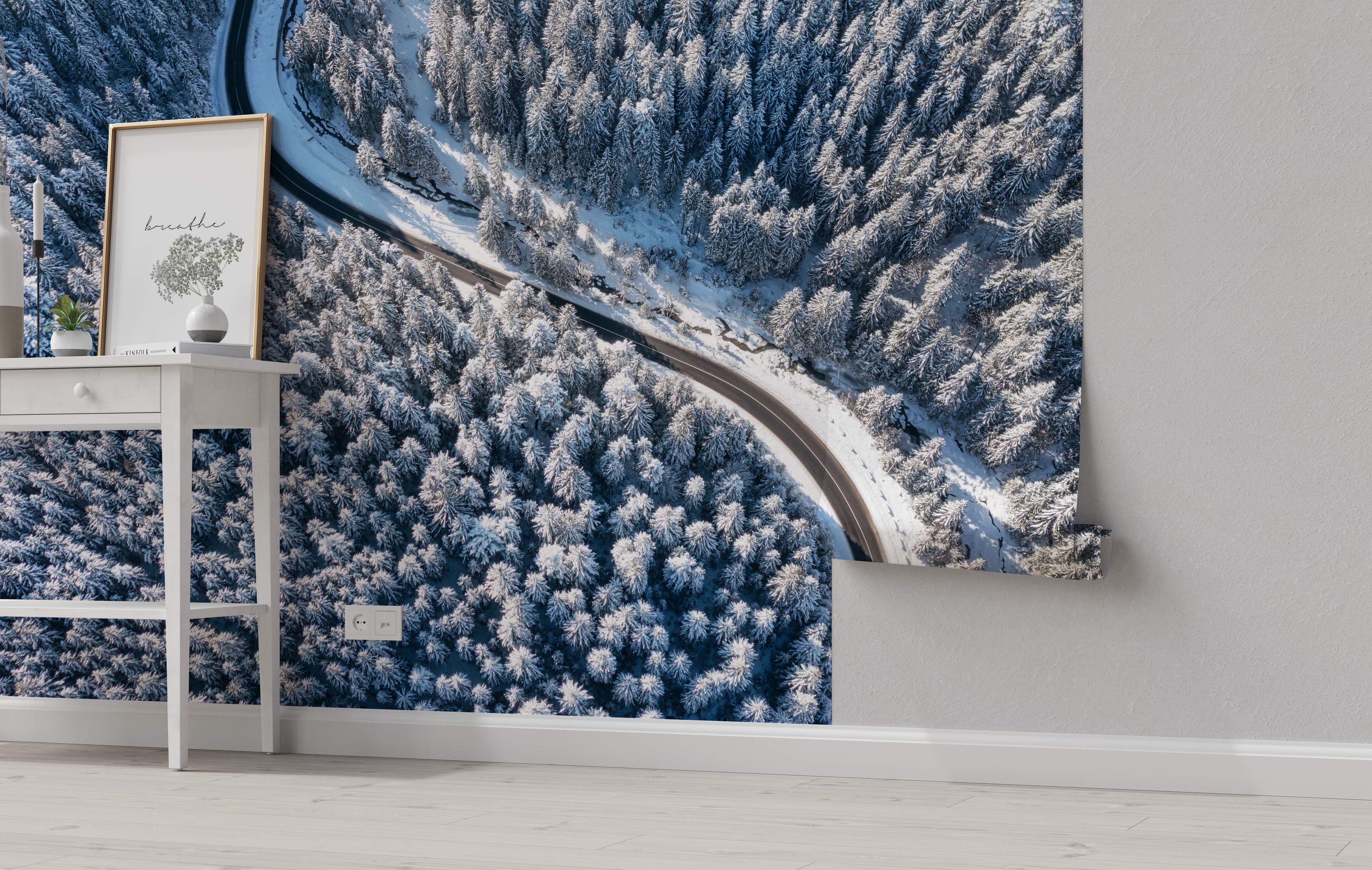 Aerial view mural of a winding road cutting through a dense, snow-covered pine forest landscape.