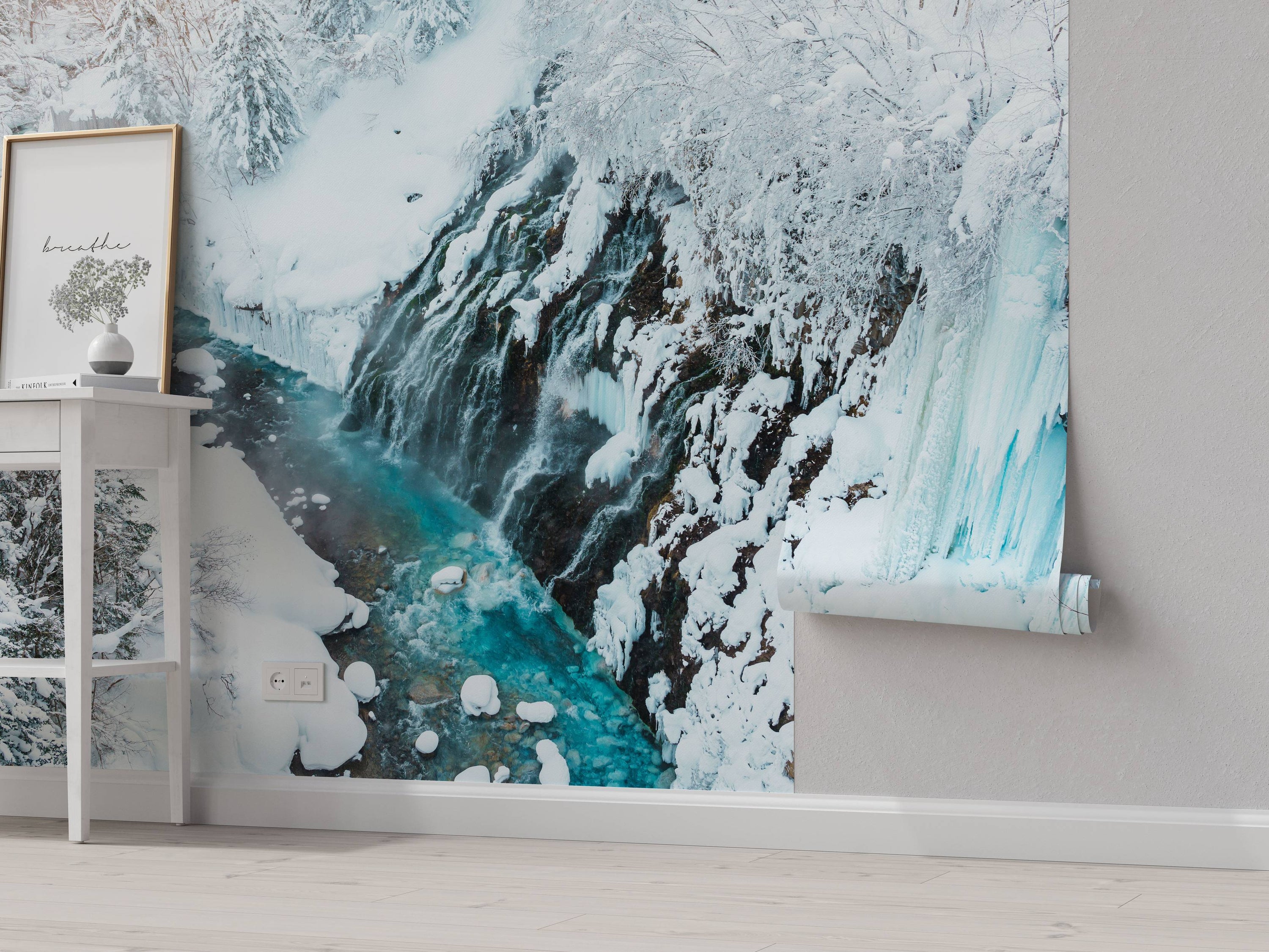 A scenic wall mural of a waterfall in winter. Turquoise water flows down a dark, rocky cliff covered in white snow and icicles.